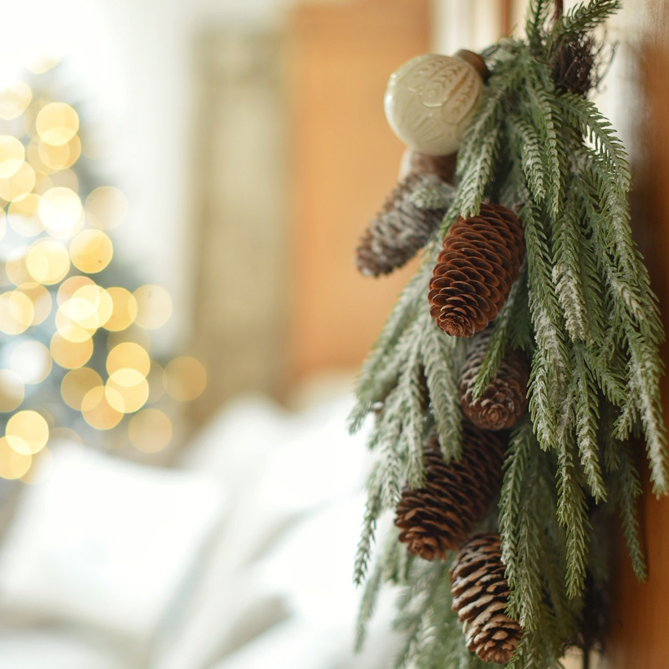 Kerstdecoratie met groene takken en bruine dennenappels tegen een wazige lichtachtergrond