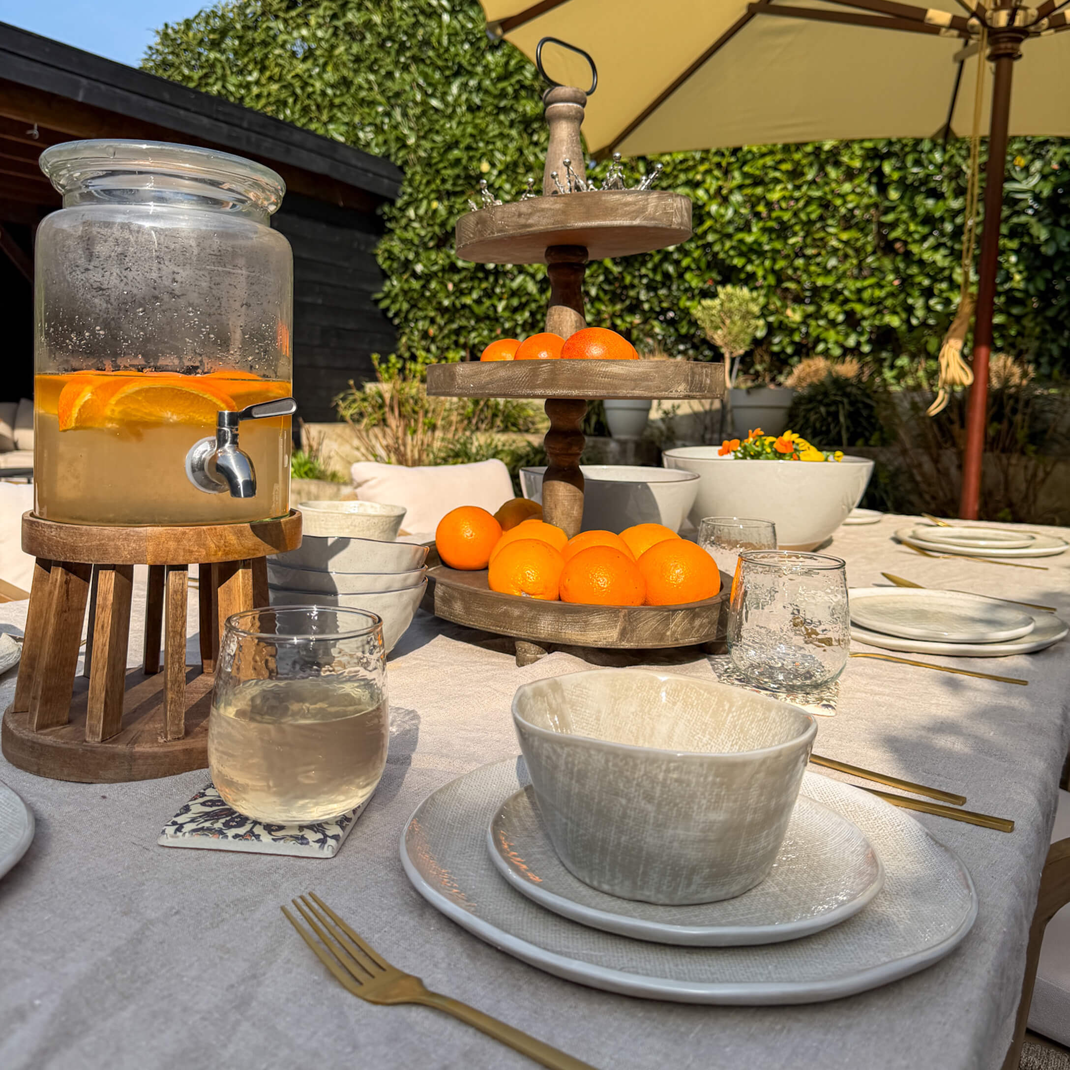 Tuin tafel met wit keramisch servies, houten fruitstandaard en kan met citrusdrank