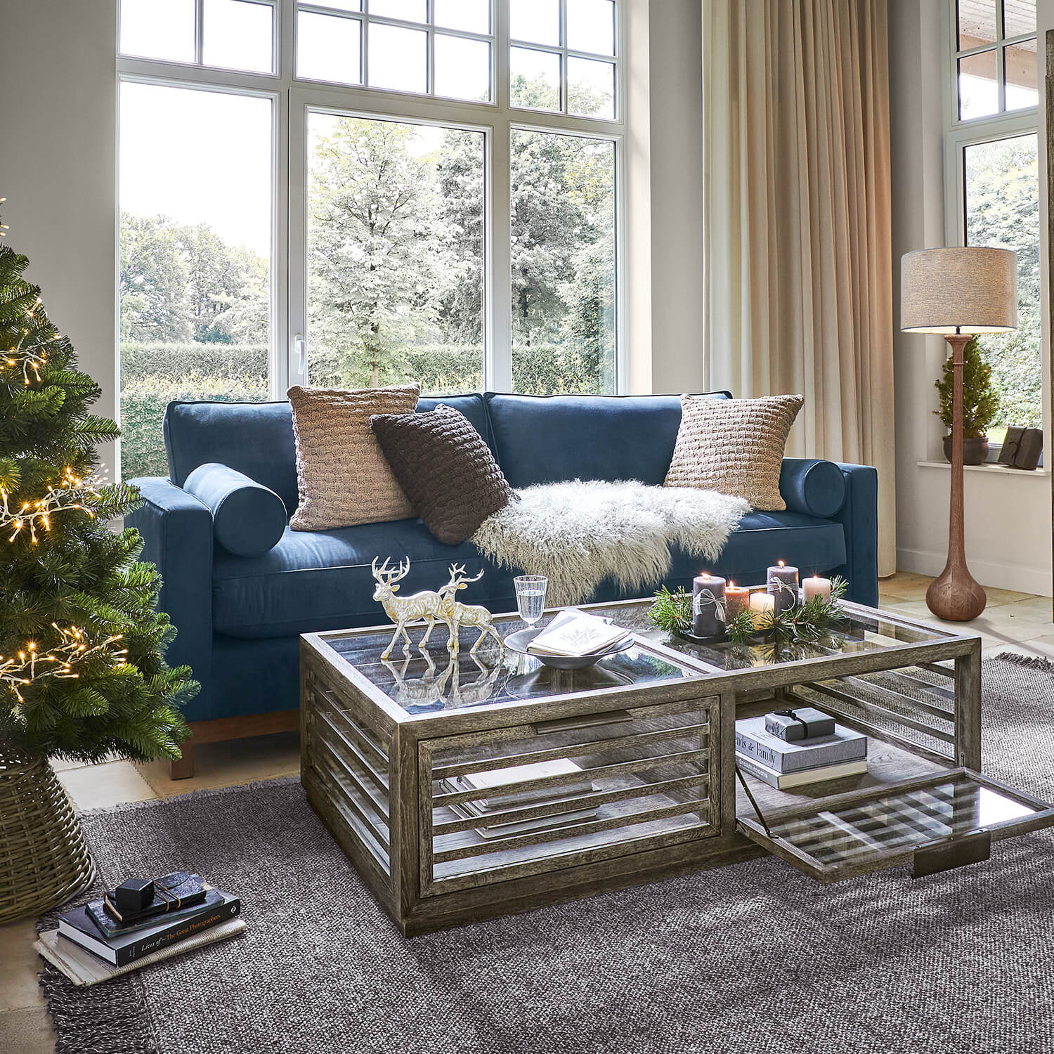 Gezellige woonkamer met donkerblauwe bank, glazen salontafel en kerstdecoratie met boom en kaarsen