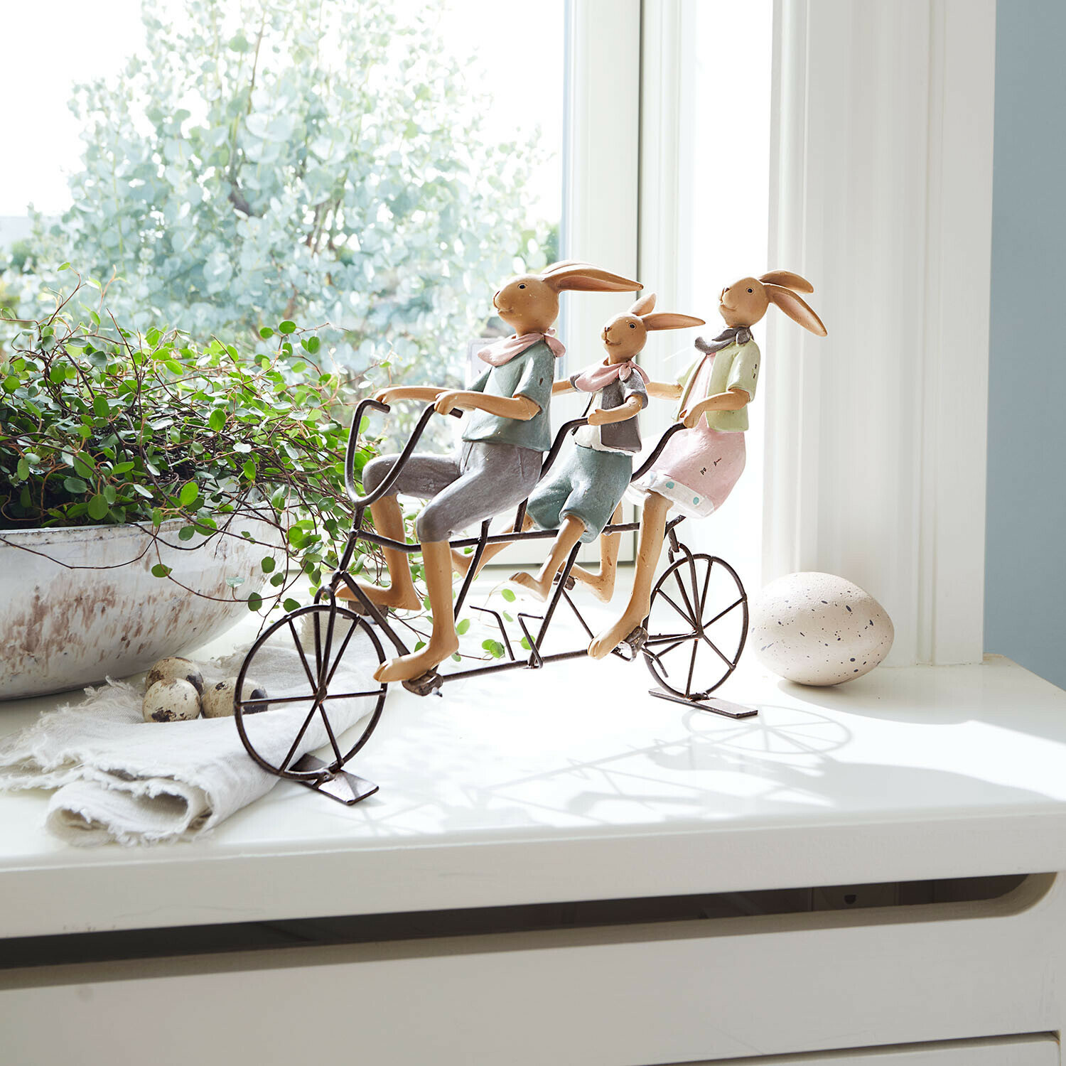 Decoratie van drie konijnen op een metalen fiets in pasteltinten op vensterbank met plant