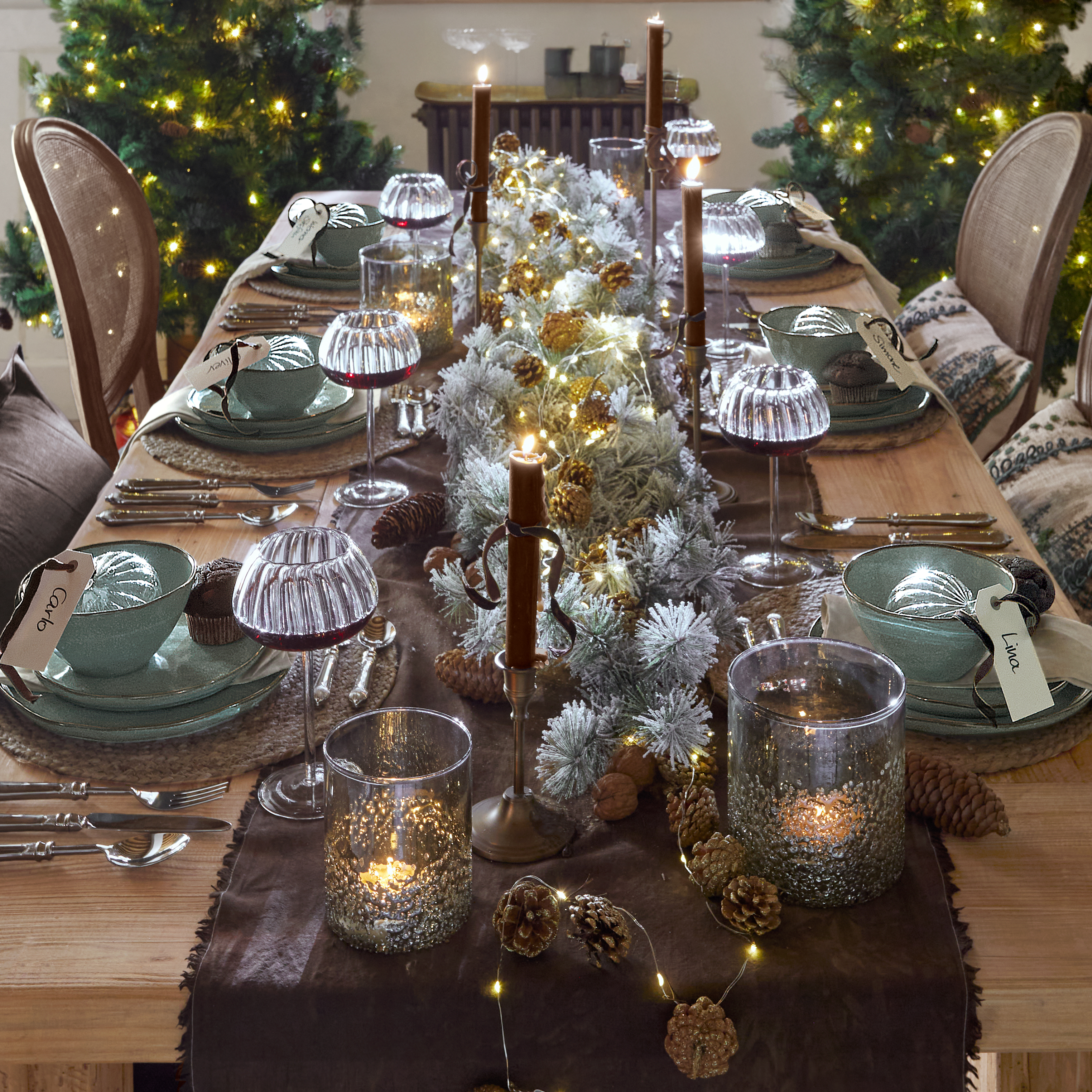 Kersttafel met groene keramische borden, brandende kaarsen en LED-lichtjes op houten tafelblad