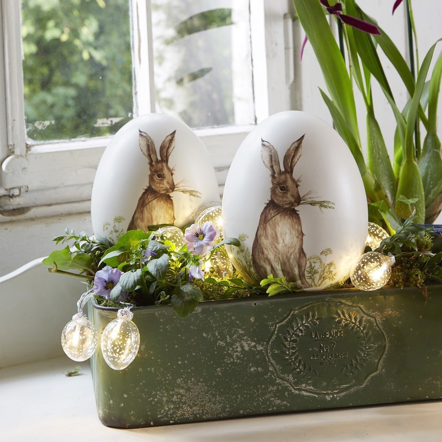 Paasei set van 2 Rubie Witte decoratieve eieren met konijnprint in groene plantenbak met bloemen en LED-lichtjes