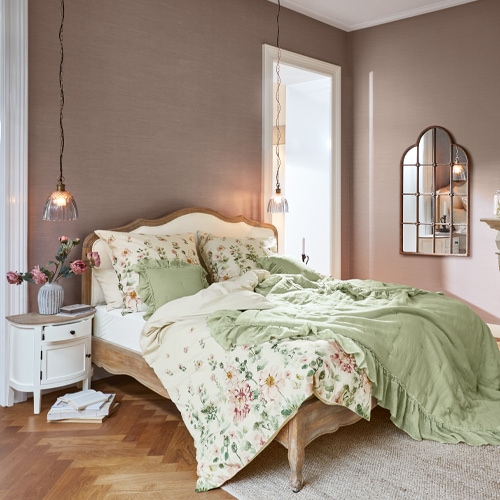 Slaapkamer met houten bed, bloemenbedlinnen en groene deken in rustieke stijl