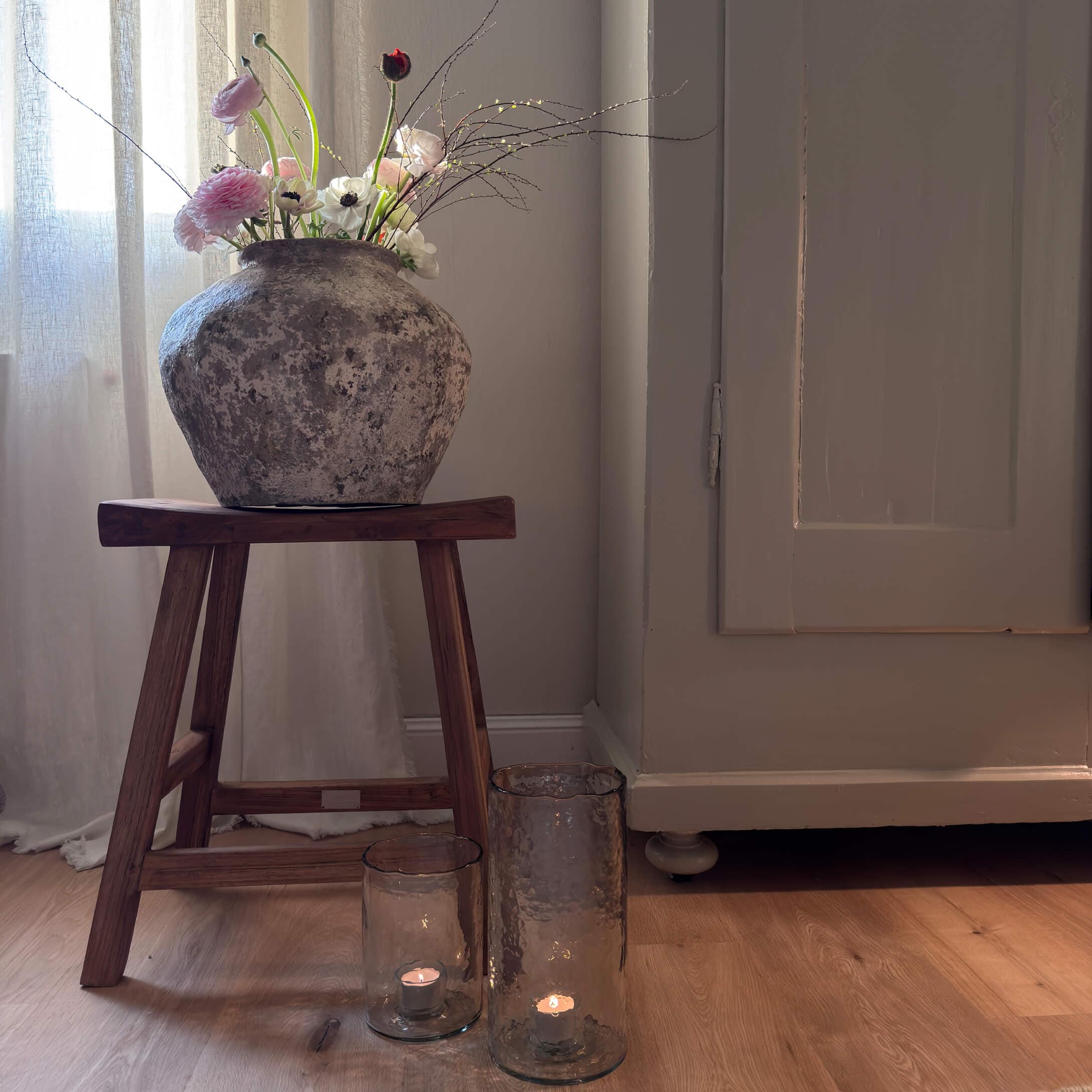Rustieke stenen vaas met bloemen op een houten kruk naast kaarsen in glazen lantaarns