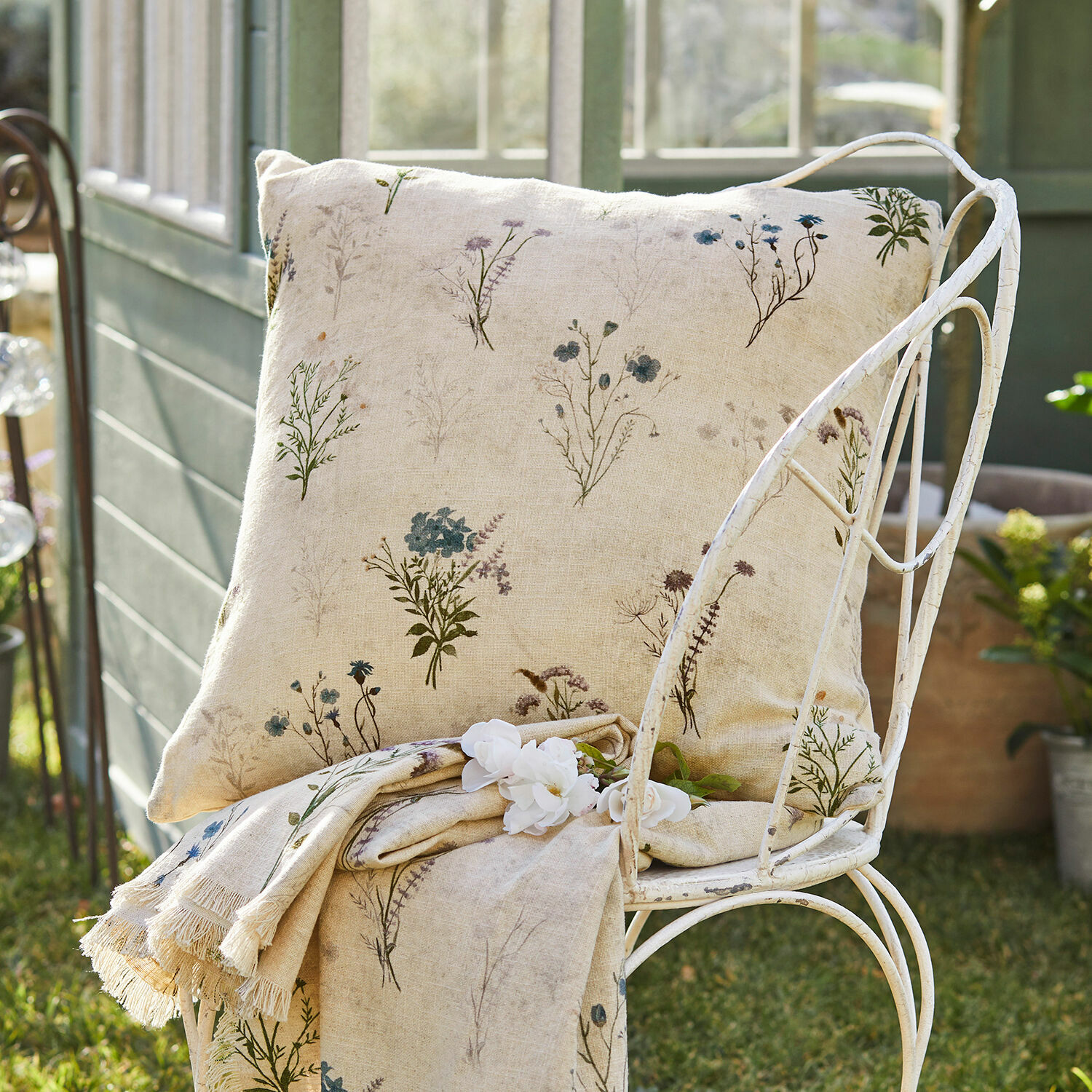 Beige linnen kussen en deken met fijn bloemenpatroon op metalen stoel in de tuin