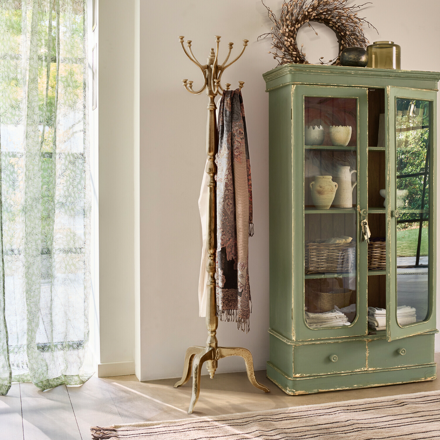 Gouden kapstok met decoratieve sjaal naast groene houten kast met glazen deuren