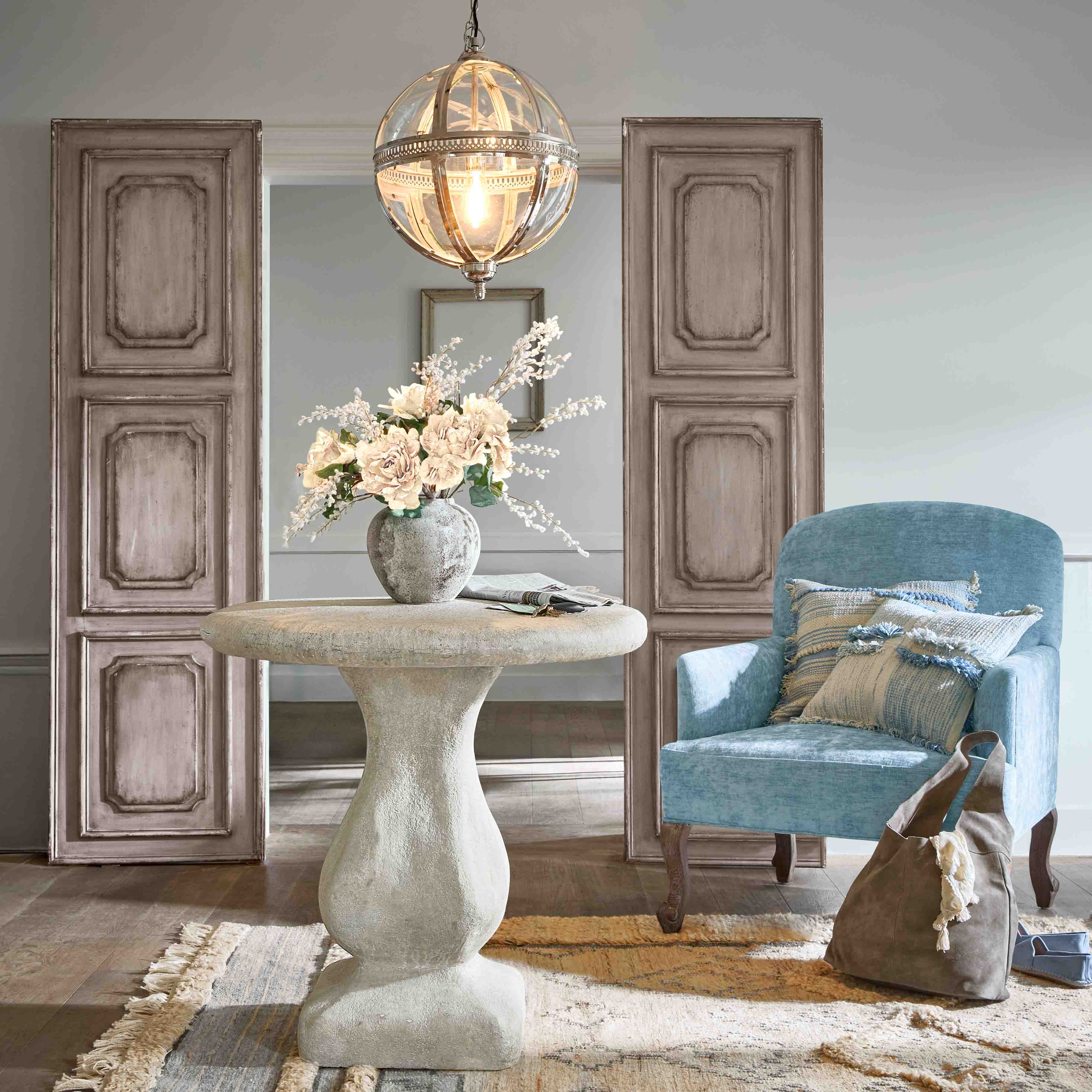 Ronde betonnen tafel met bloemenvaas en blauwe fauteuil met kussens in stijlvolle woonkamer