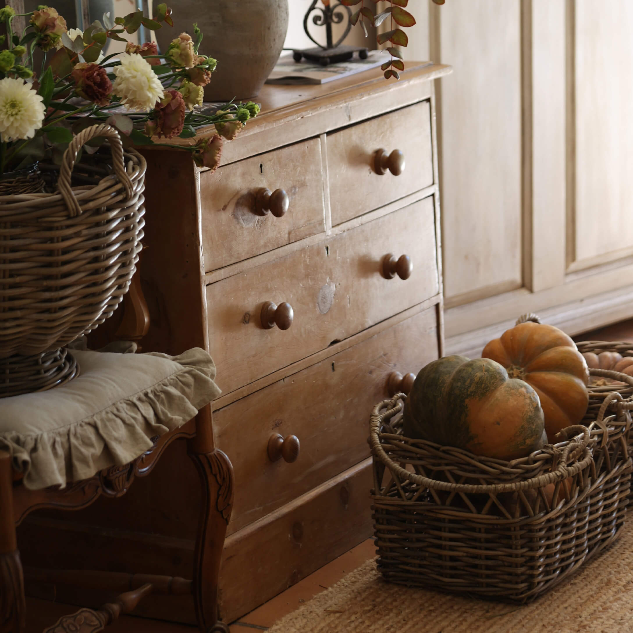 Rustieke houten ladekast met vier lades en een rieten mand met pompoenen in een gezellige kamer