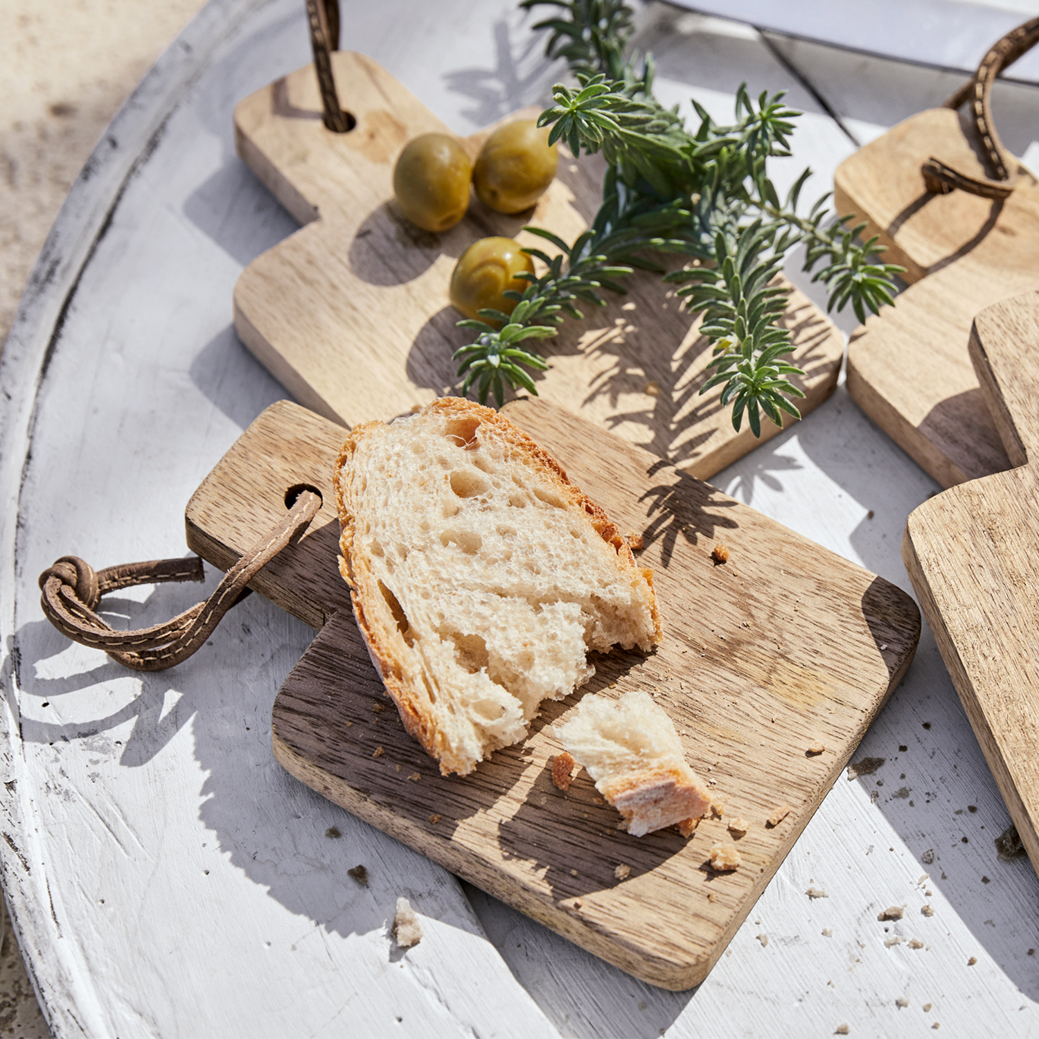 Houten snijplank met stuk brood, groene olijven en kruiden op een witte tafel