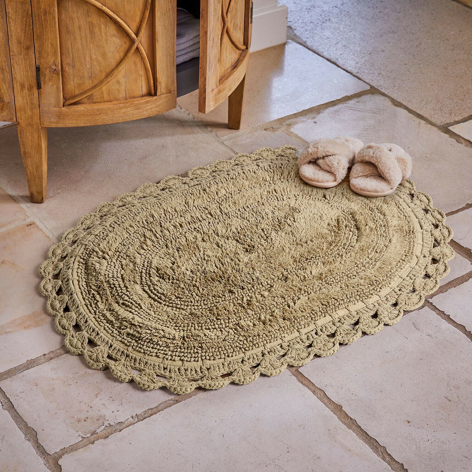 Ovale beige katoenen vloerkleed met decoratieve rand op stenen vloer met pantoffels