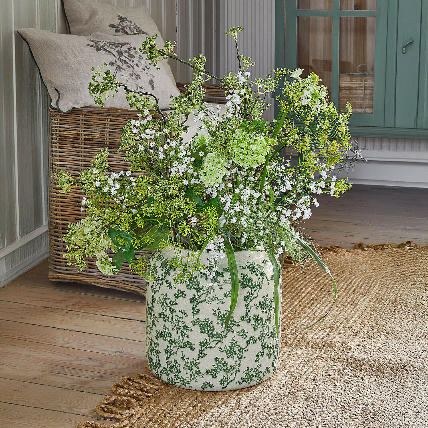 Witte keramische vaas met groen patroon, witte bloemen en groene takken op houten vloer