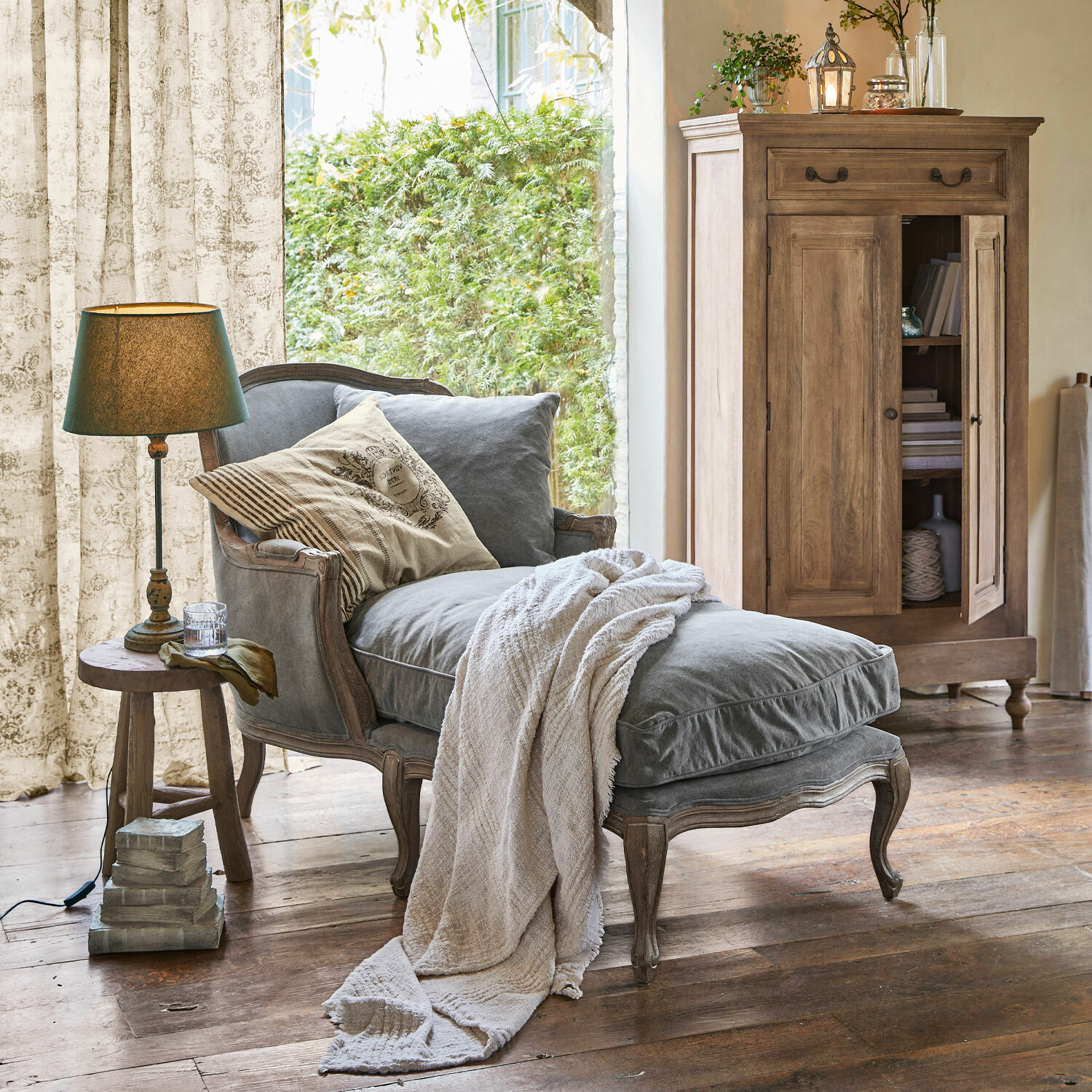 Chaise longue Muel Grijze gestoffeerde chaise longue met houten frame en beige deken in rustieke woonkamer