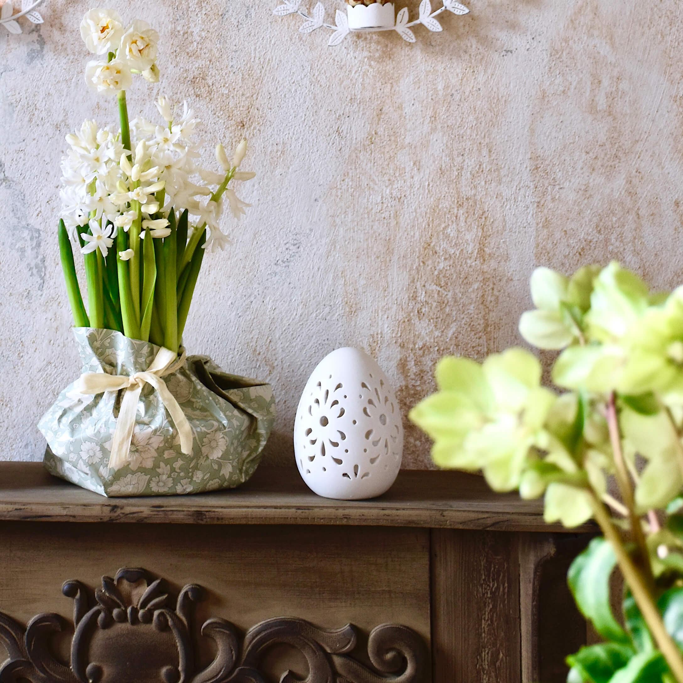 Witte bloemen in groene decoratieve verpakking en wit keramisch ei op houten plank