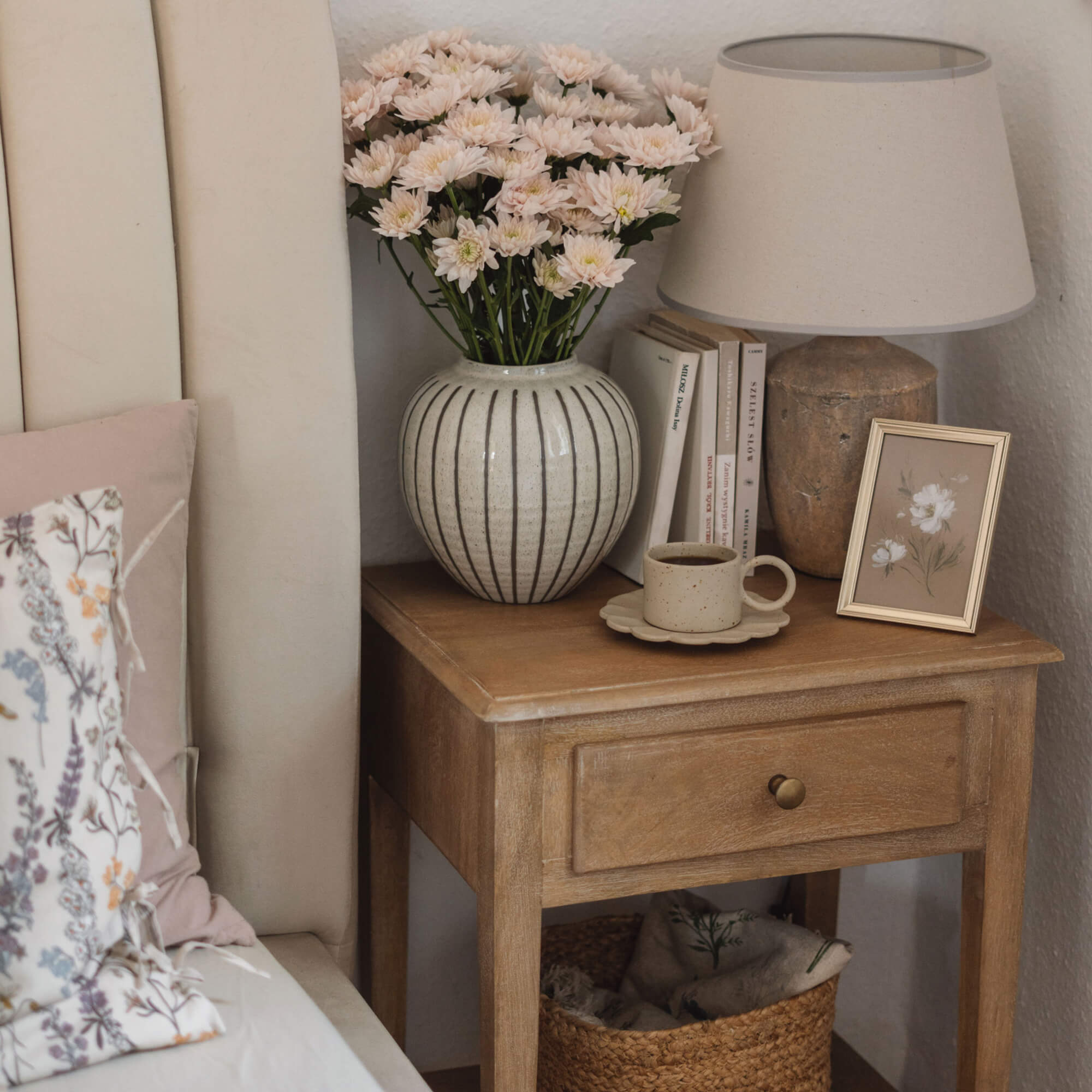 Houten nachtkastje met keramische lamp, bloemenvaas en koffiekopje in gezellige slaapkamer