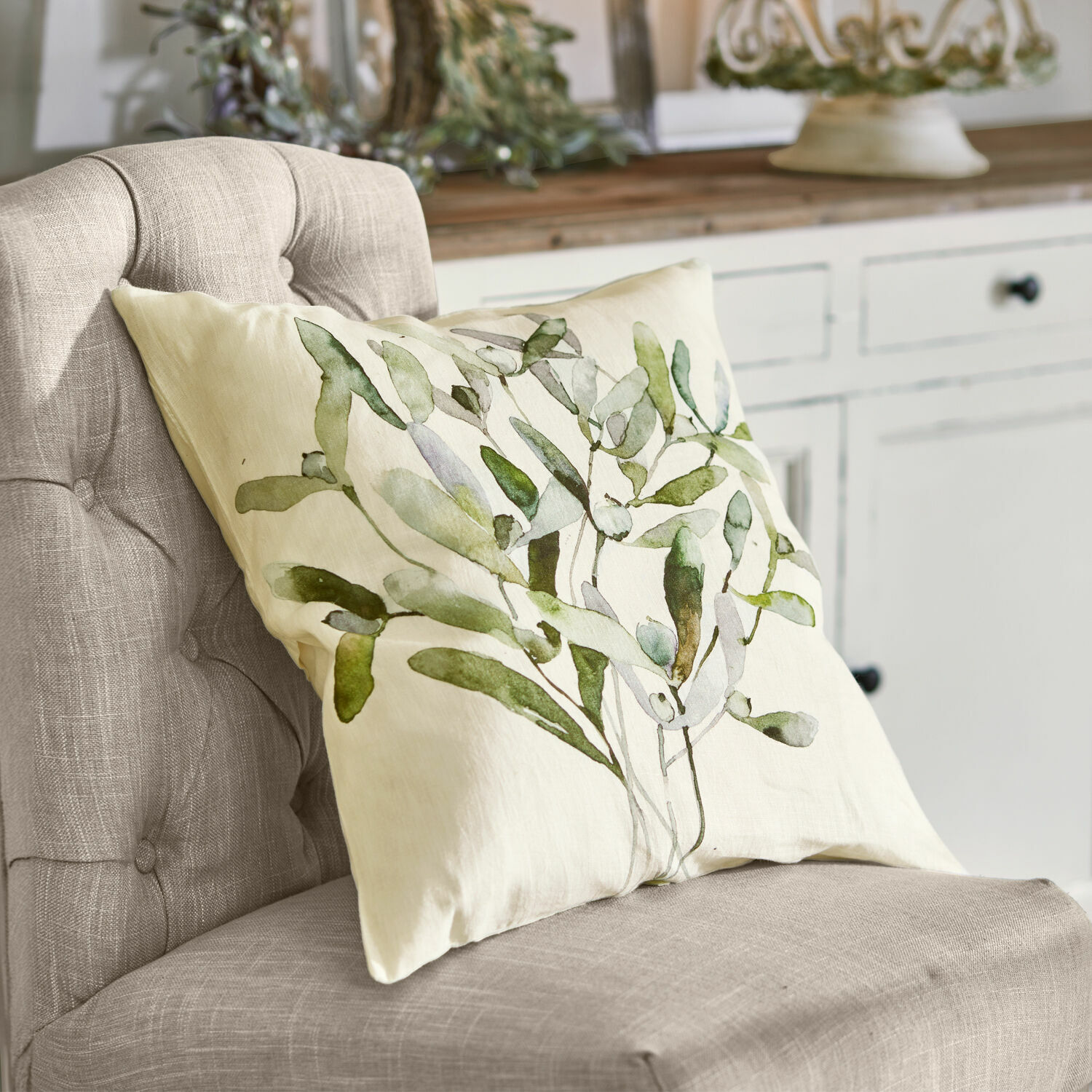 Kussenhoes Mistletoe Beige sierkussen met groen bladmotief op grijze stoel in natuurlijke stijl