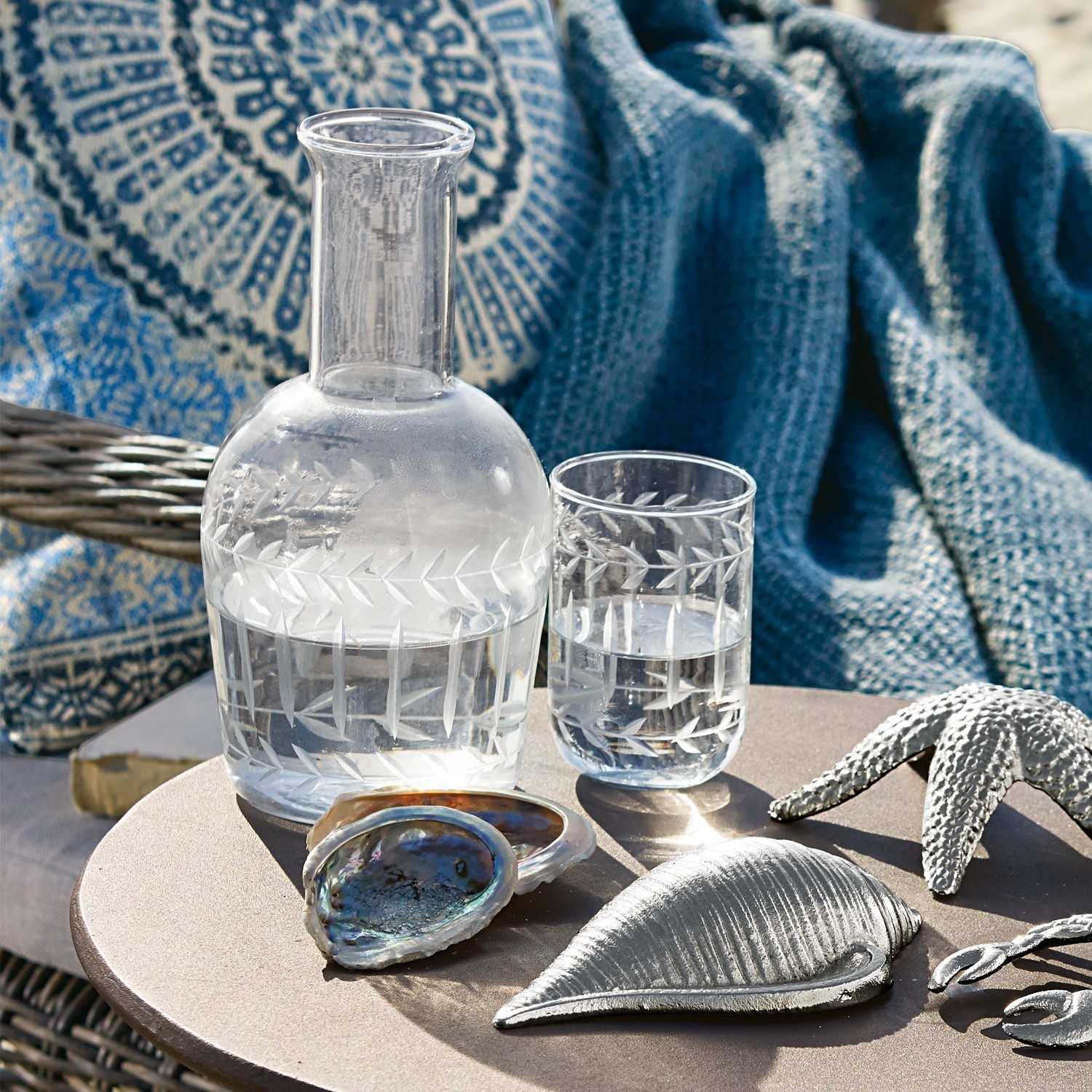 Glazen karaf en glas met gegraveerd patroon op tafel met schelpen- en zeesterdecoratie