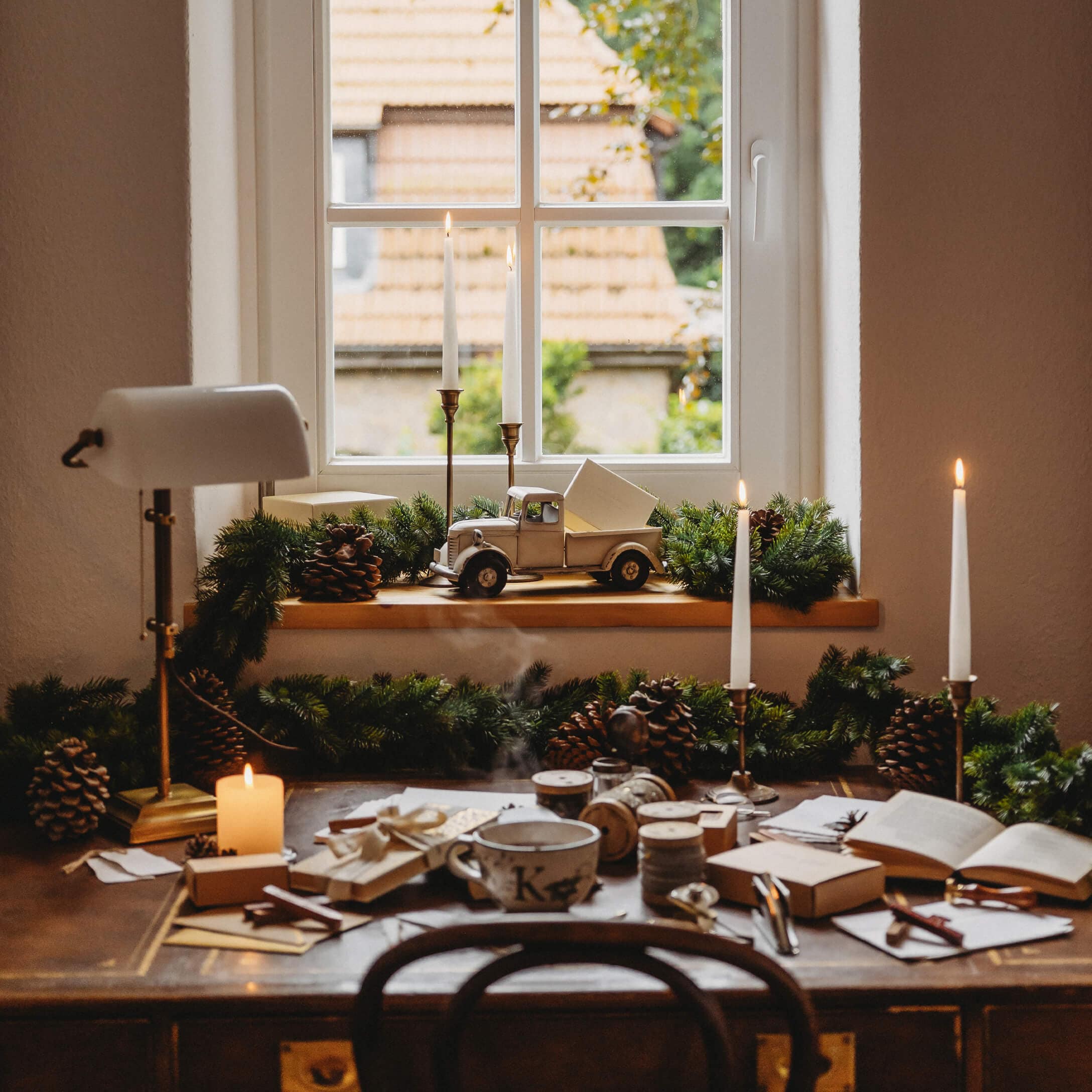 Rustieke houten tafel met kaarsen en kerstdecoratie bij raam met uitzicht op daken