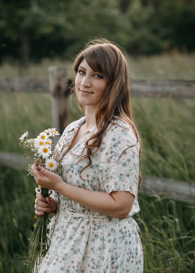 Vrouw in bloemenjurk met boeket madeliefjes voor groen veld en houten hek