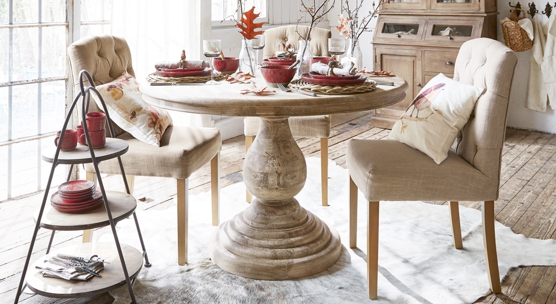 Lichte houten ronde tafel met beige gestoffeerde stoelen in gezellige eetkamer met decoratie