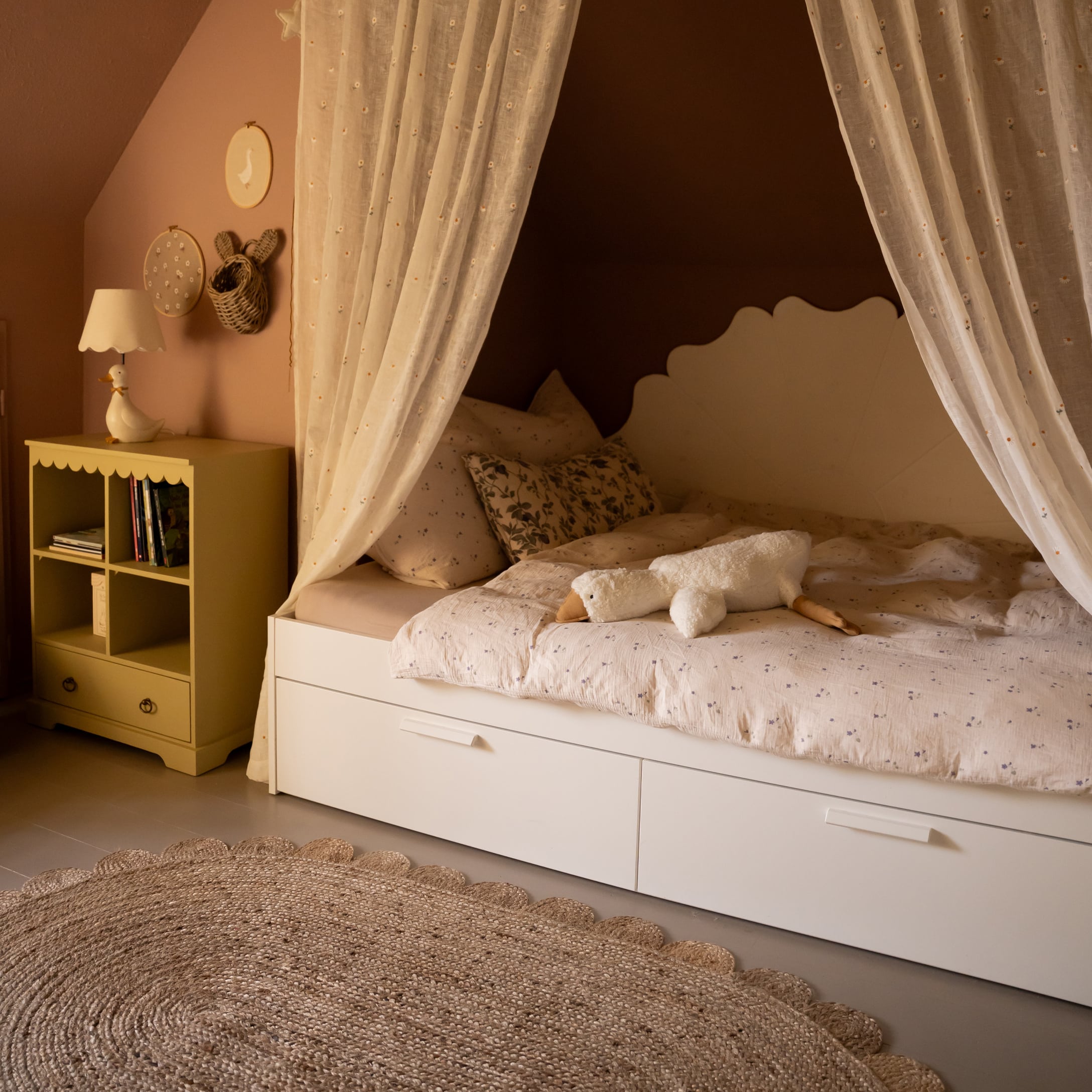 Gezellig kinderbed met wit frame, lichte gordijnen en een knuffelgans op beddengoed met bloemenprint