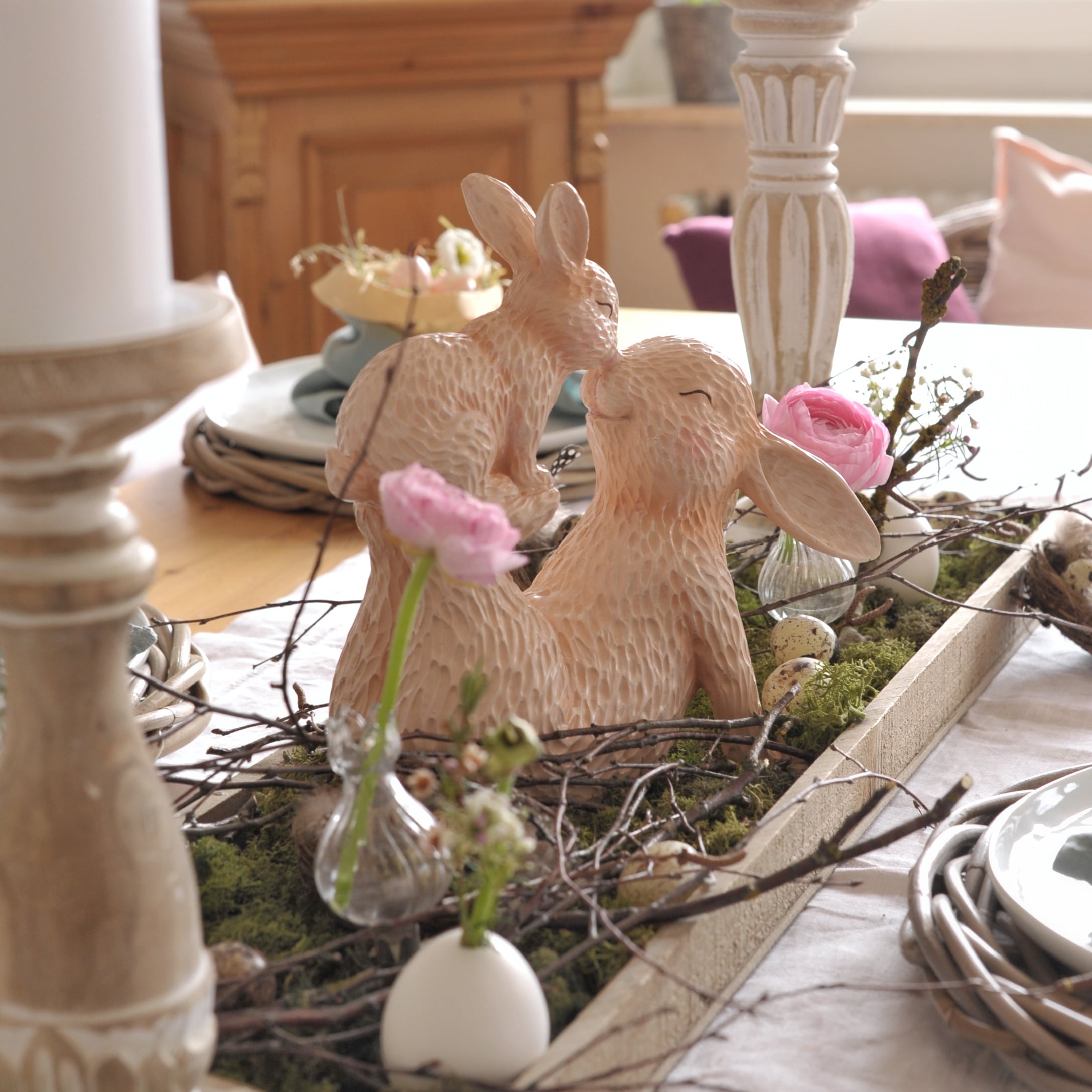 Tafelversiering met beige keramische konijnen en roze bloemen op groen mos