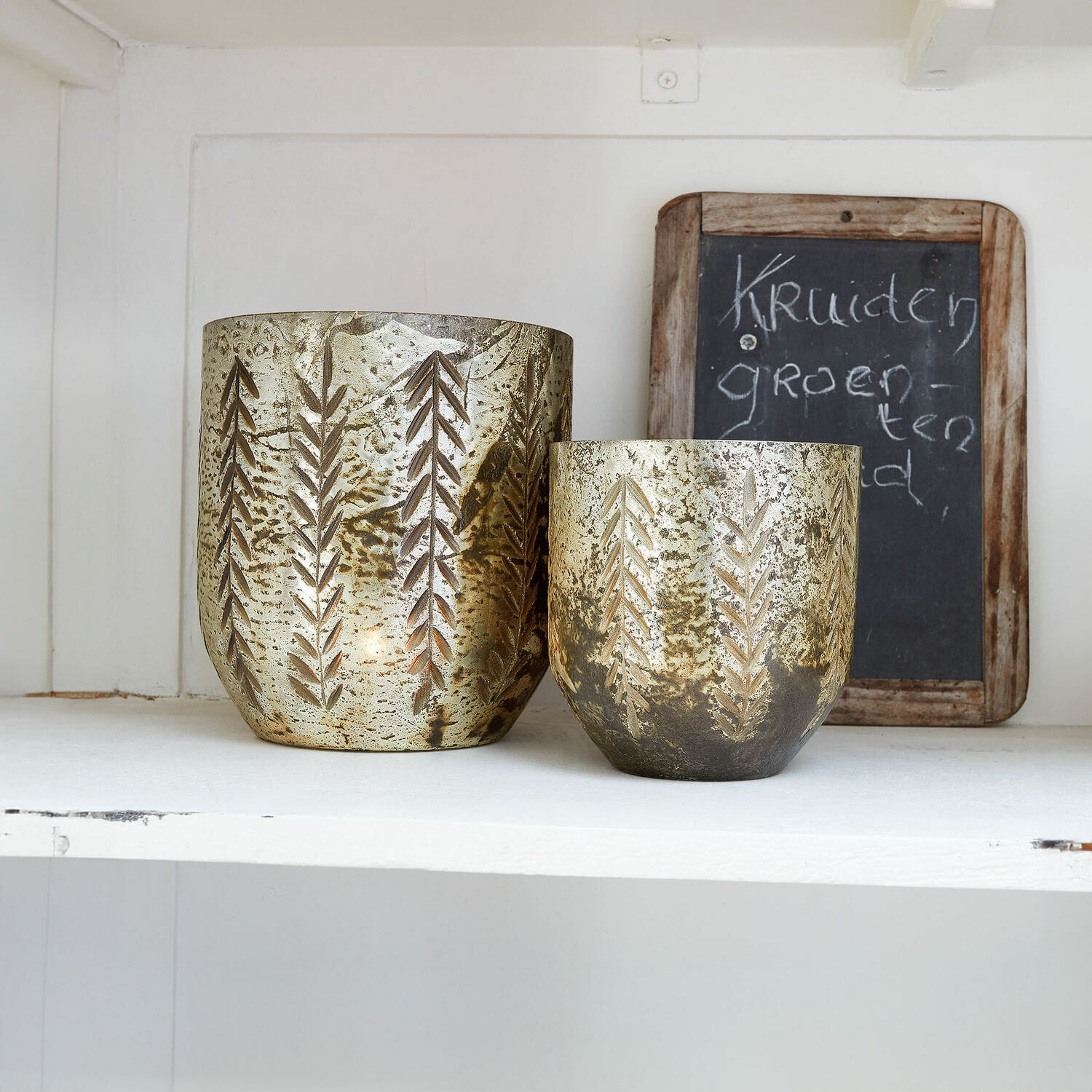 Windlicht set van 2 Filorex Set van twee gouden metalen theelichthouders met bladpatroon op witte plank, interieurdecoratie