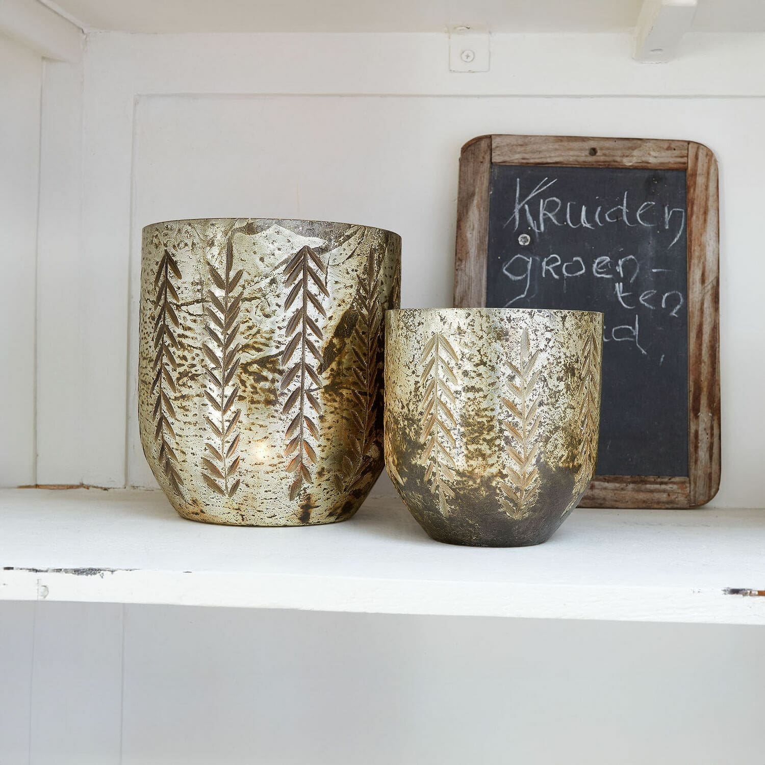 Windlicht set van 2 Filorex Set van twee gouden metalen theelichthouders met bladpatroon op witte plank, interieurdecoratie
