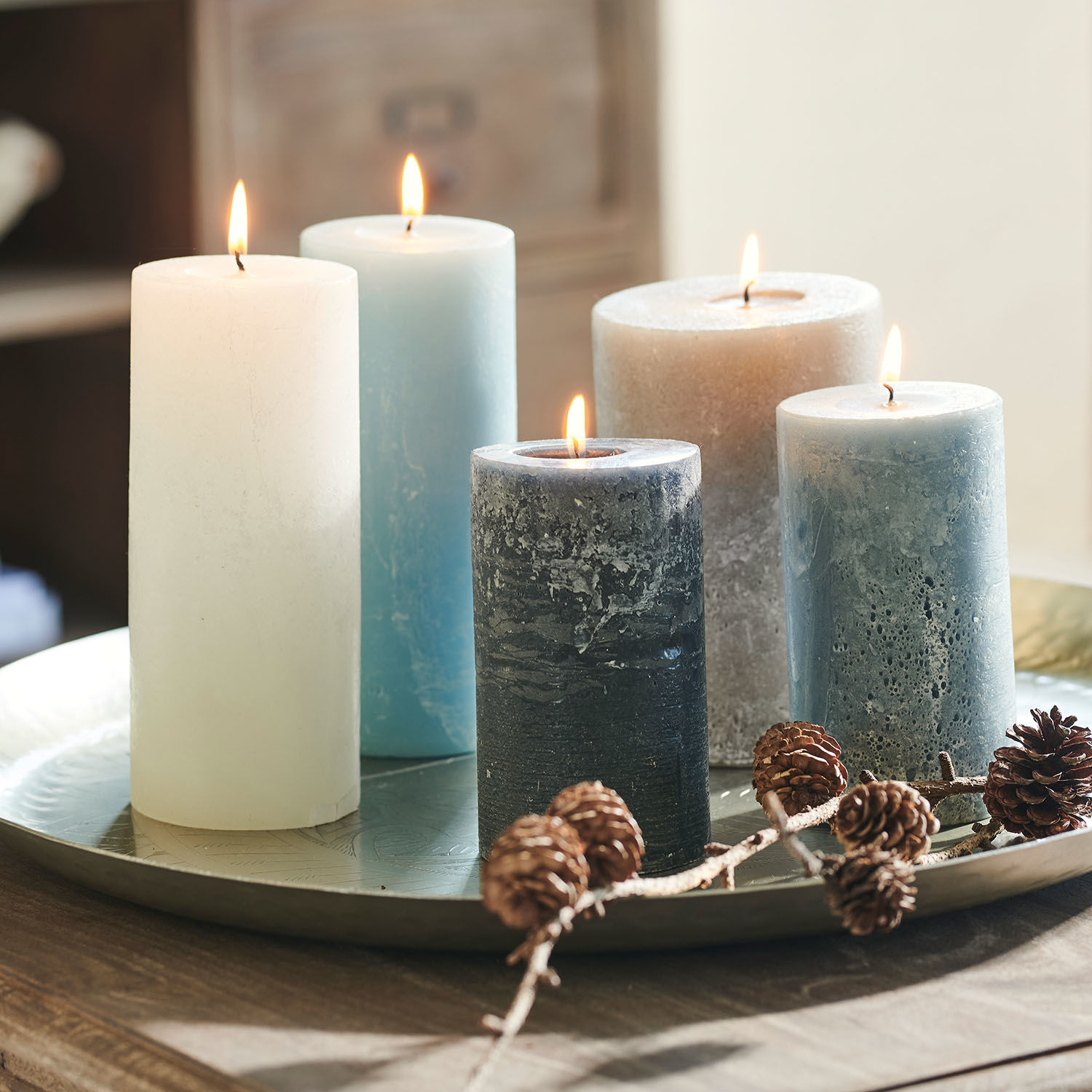 Set van vijf kaarsen in verschillende blauw- en wit tinten op metalen schaal met dennenappels