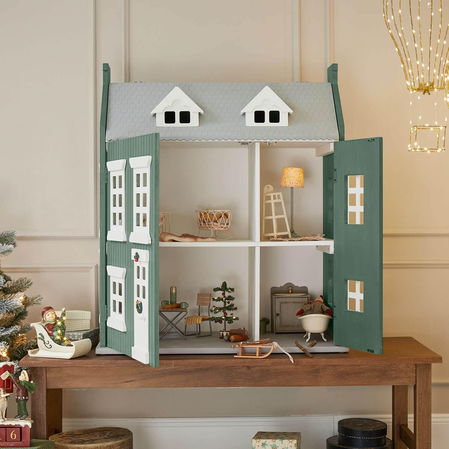Houten poppenhuis in groen en grijs met open deuren en kerstdecoratie binnenin