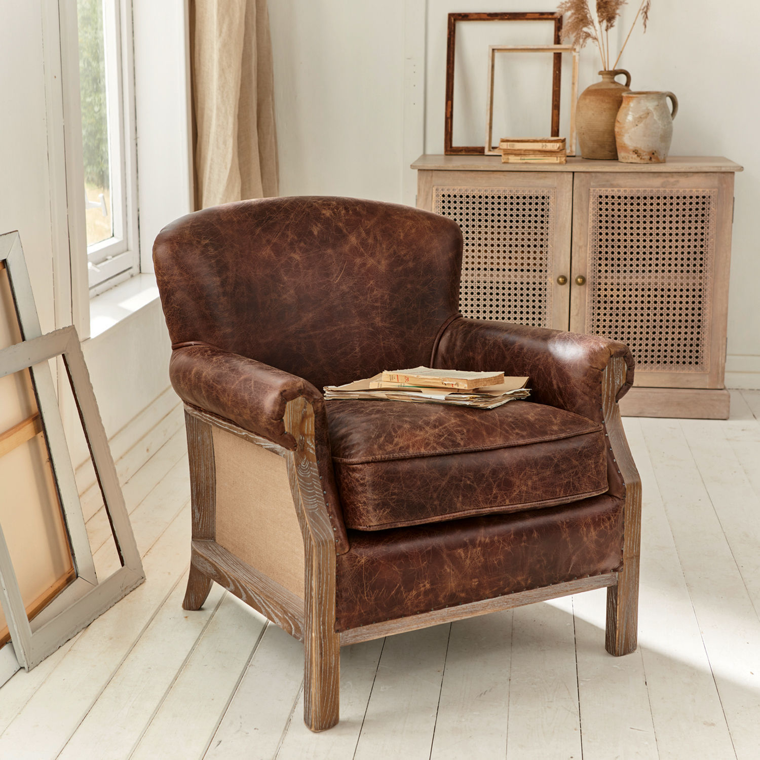 Fauteuil Banbury Bruine leren fauteuil met verweerde look en houten frame in lichte kamer met natuurlijk licht