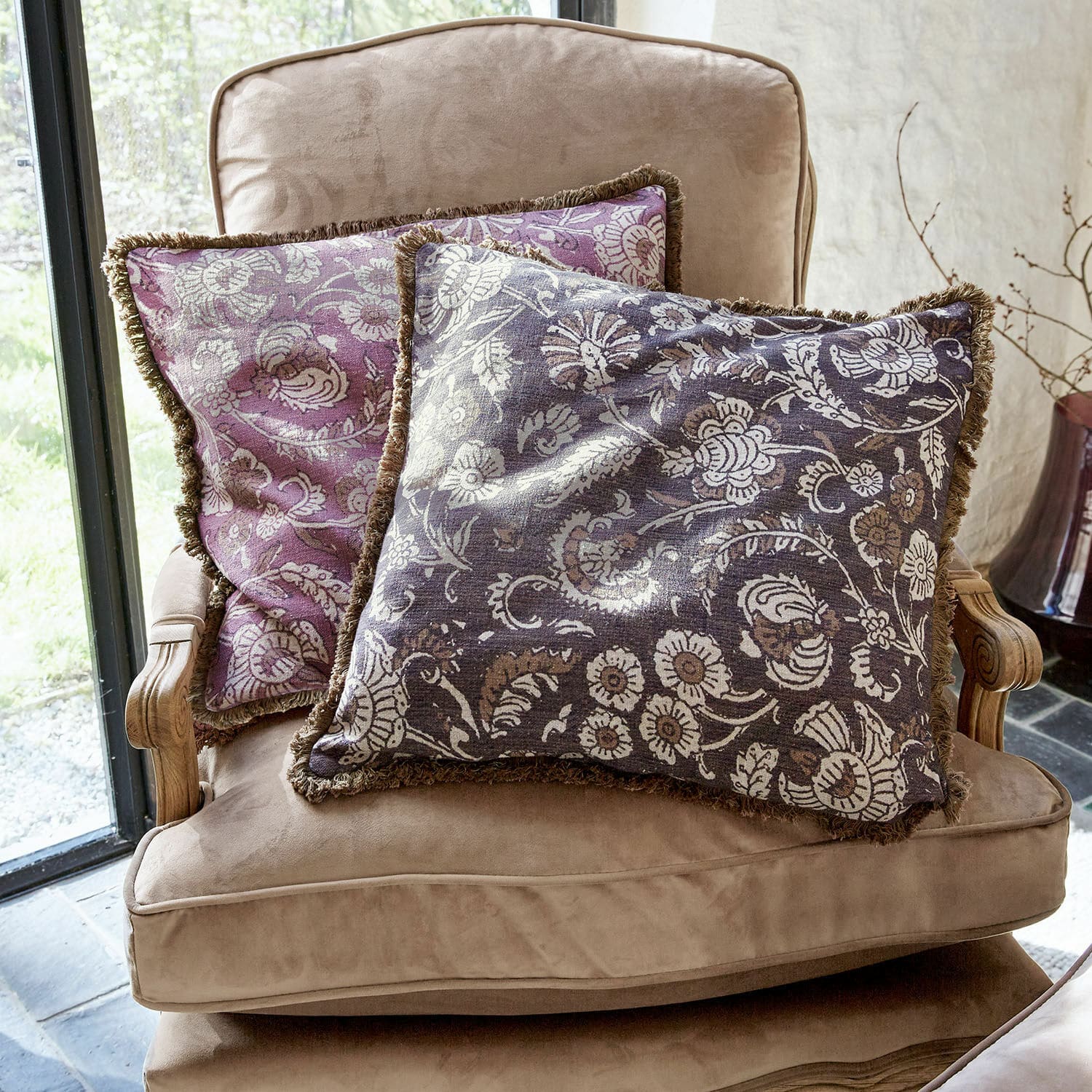 Kussenhoes set van 2 Lalluga Twee decoratieve kussens met bloemenpatroon in paars en grijs op een beige fauteuil
