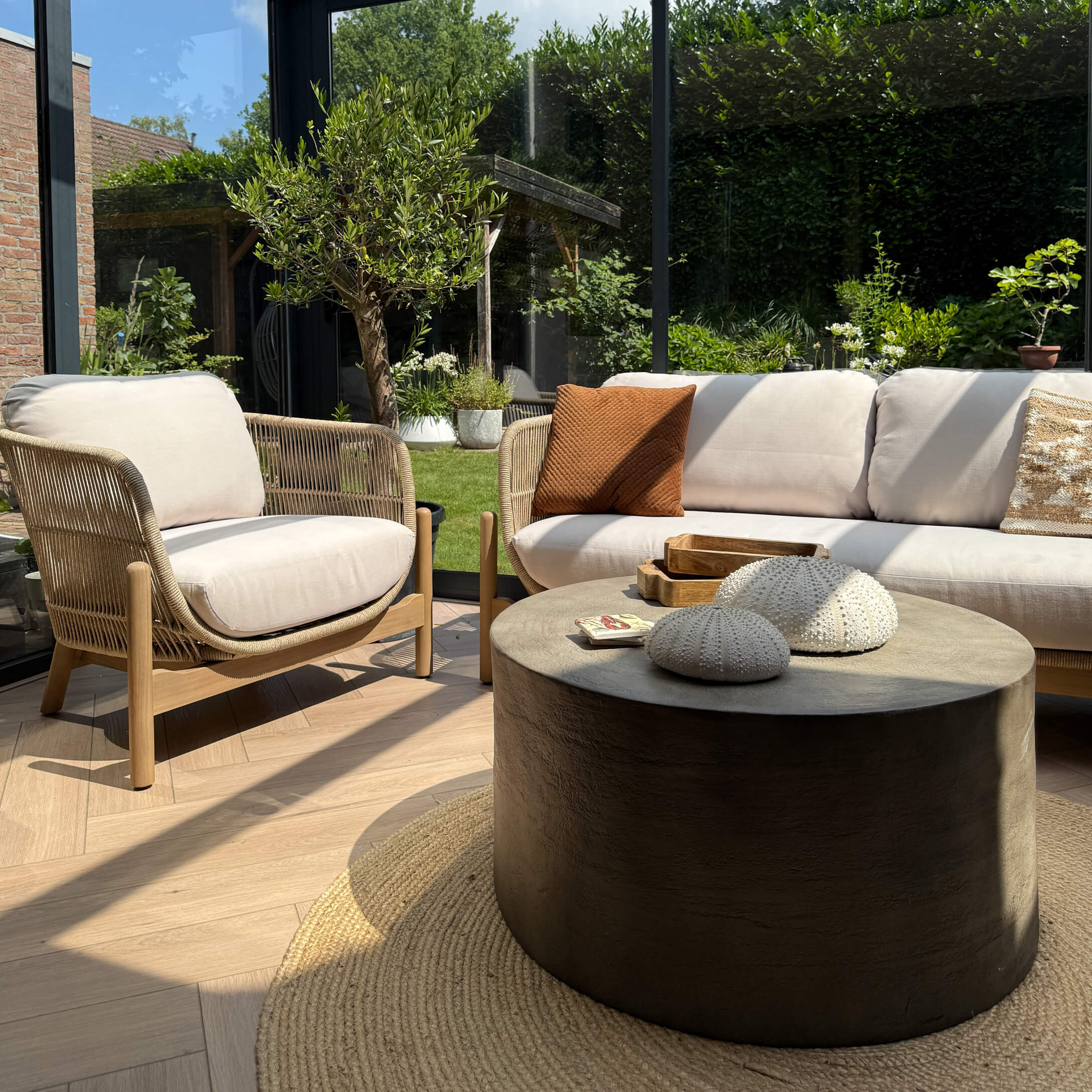 Moderne woonkamer met beige bank, houten en stoffen fauteuil en zwarte ronde salontafel met natuurlijke decoratie