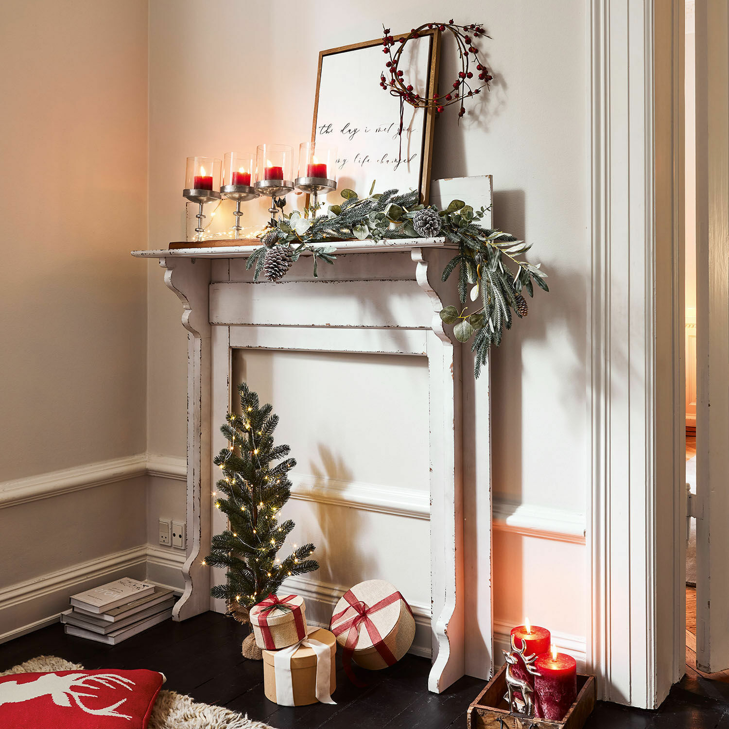 Witte decoratieve houten schouw met groene krans, rode kaarsen en kerstcadeaus