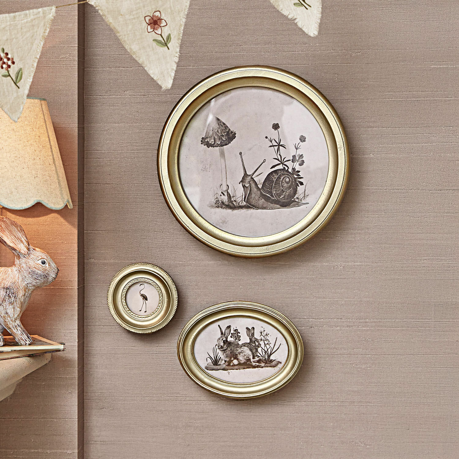 Muurdecoratie set van 3 Atriana Set van drie gouden lijsten met zwart-witte illustraties van dieren en planten aan een beige muur.