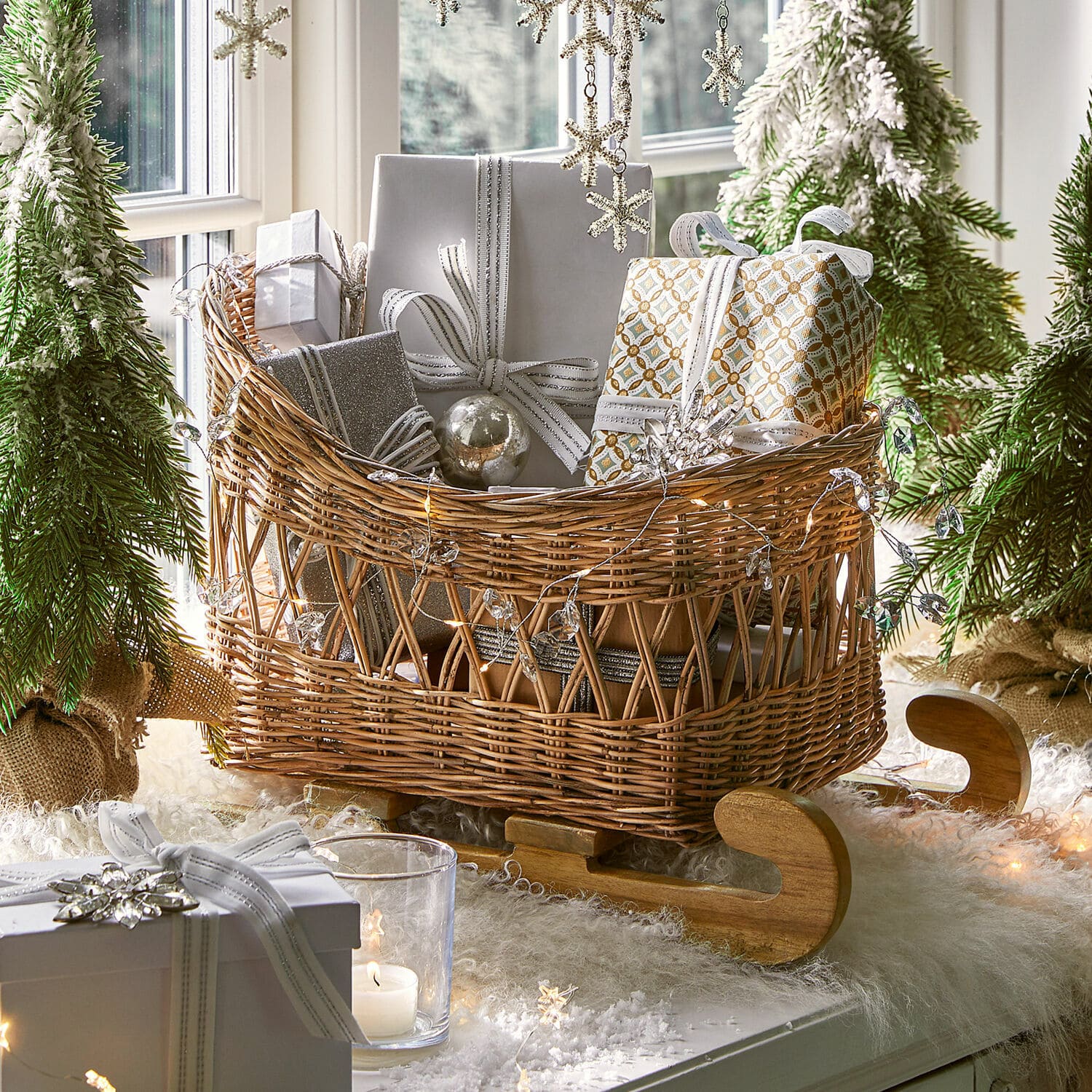 Rieten slee met houten runners gevuld met zilver-wit ingepakte cadeaus in kerstdecoratie