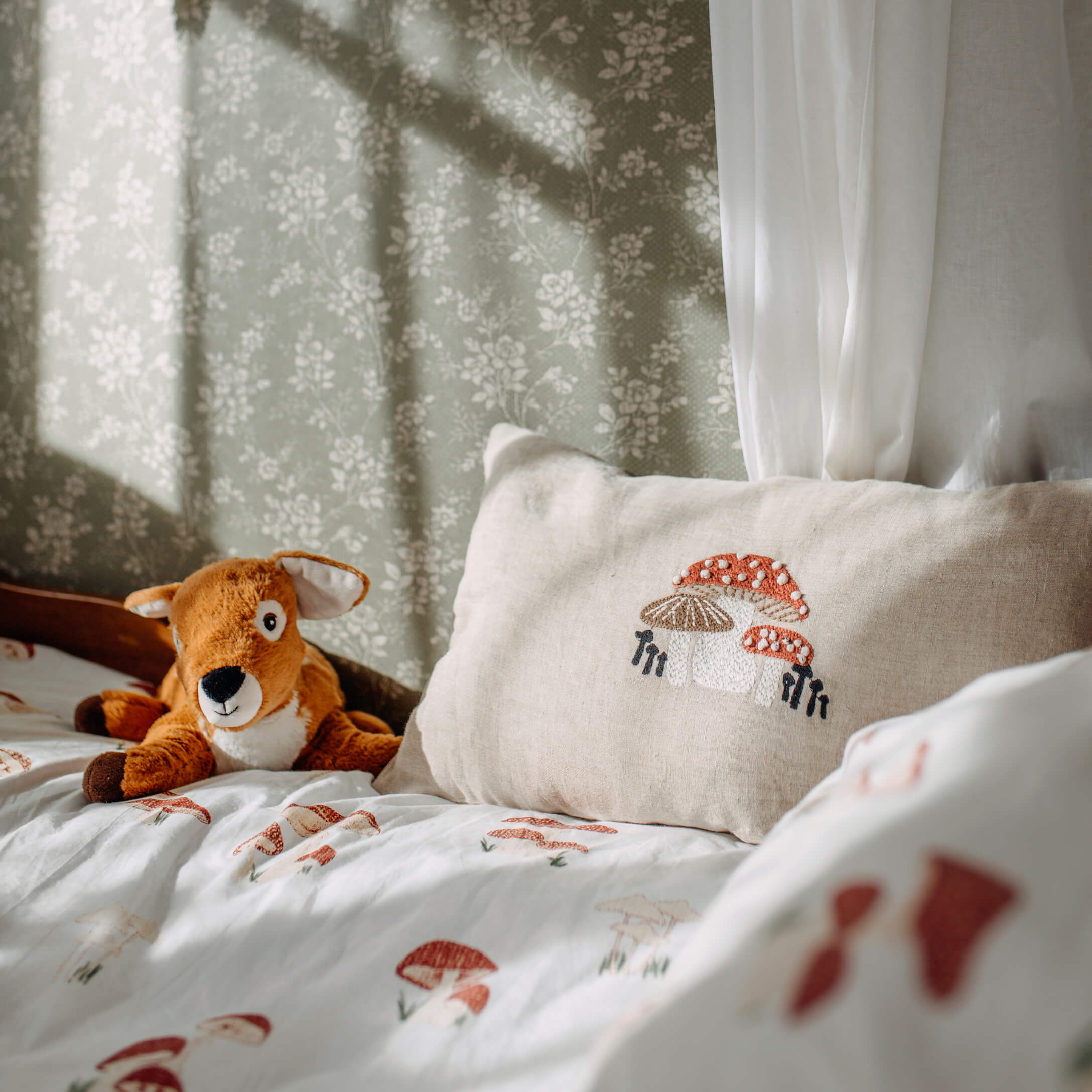 Beige linnen kussen met paddenstoel borduurwerk op bed met paddenstoelen beddengoed en een knuffel hert