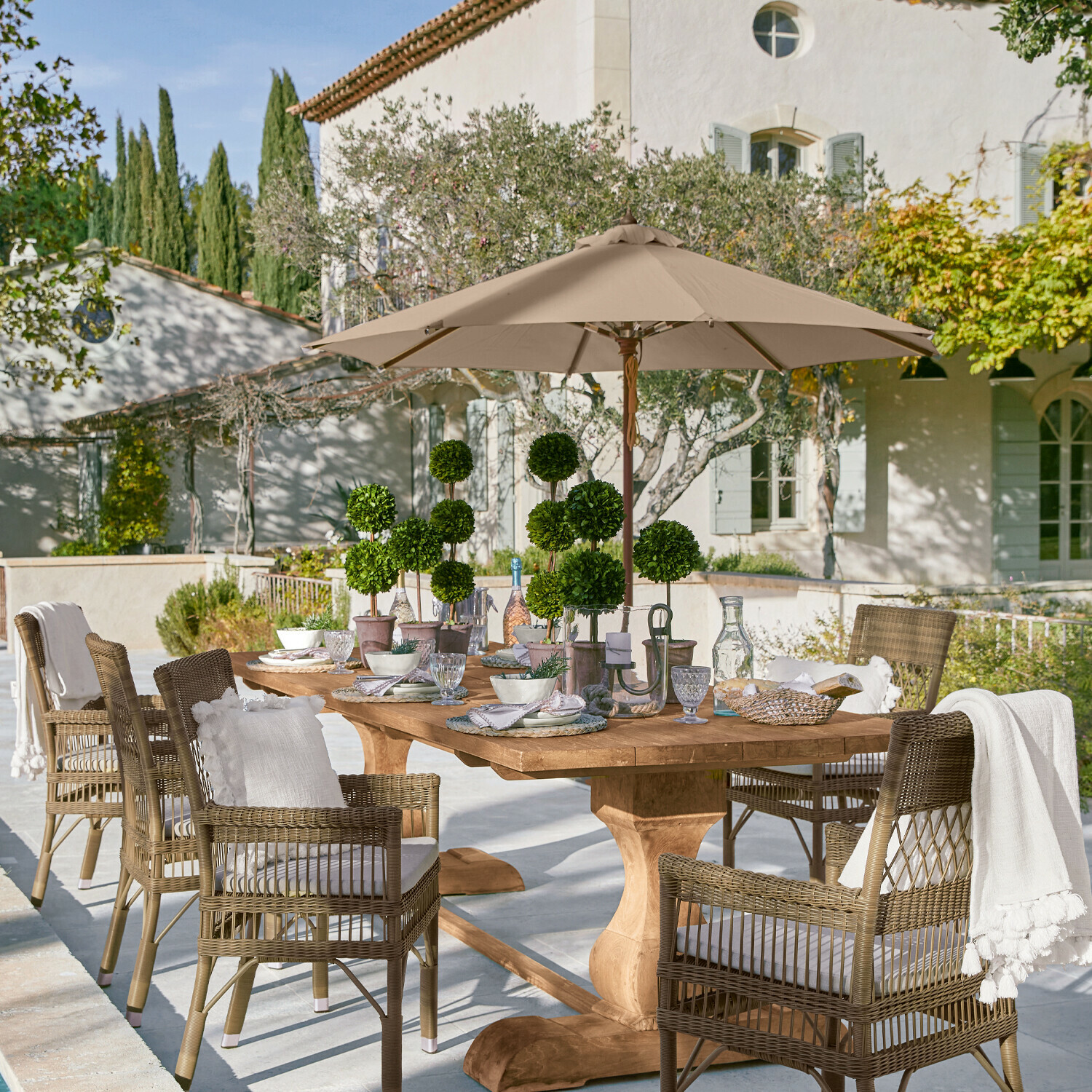 Parasol Brent Grote houten tuintafel met rieten stoelen en beige parasol op zonnig terras
