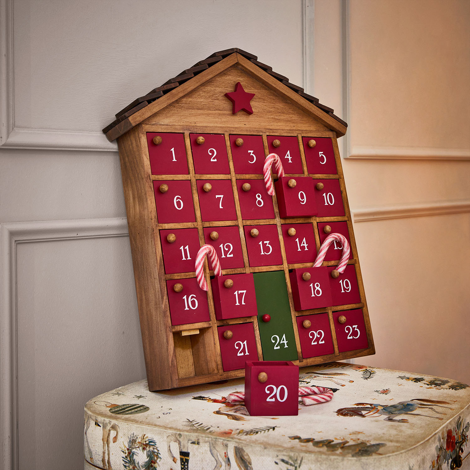 Houten adventskalender in de vorm van een huis met rode deurtjes en groene deur 24, versierd met zuurstokken