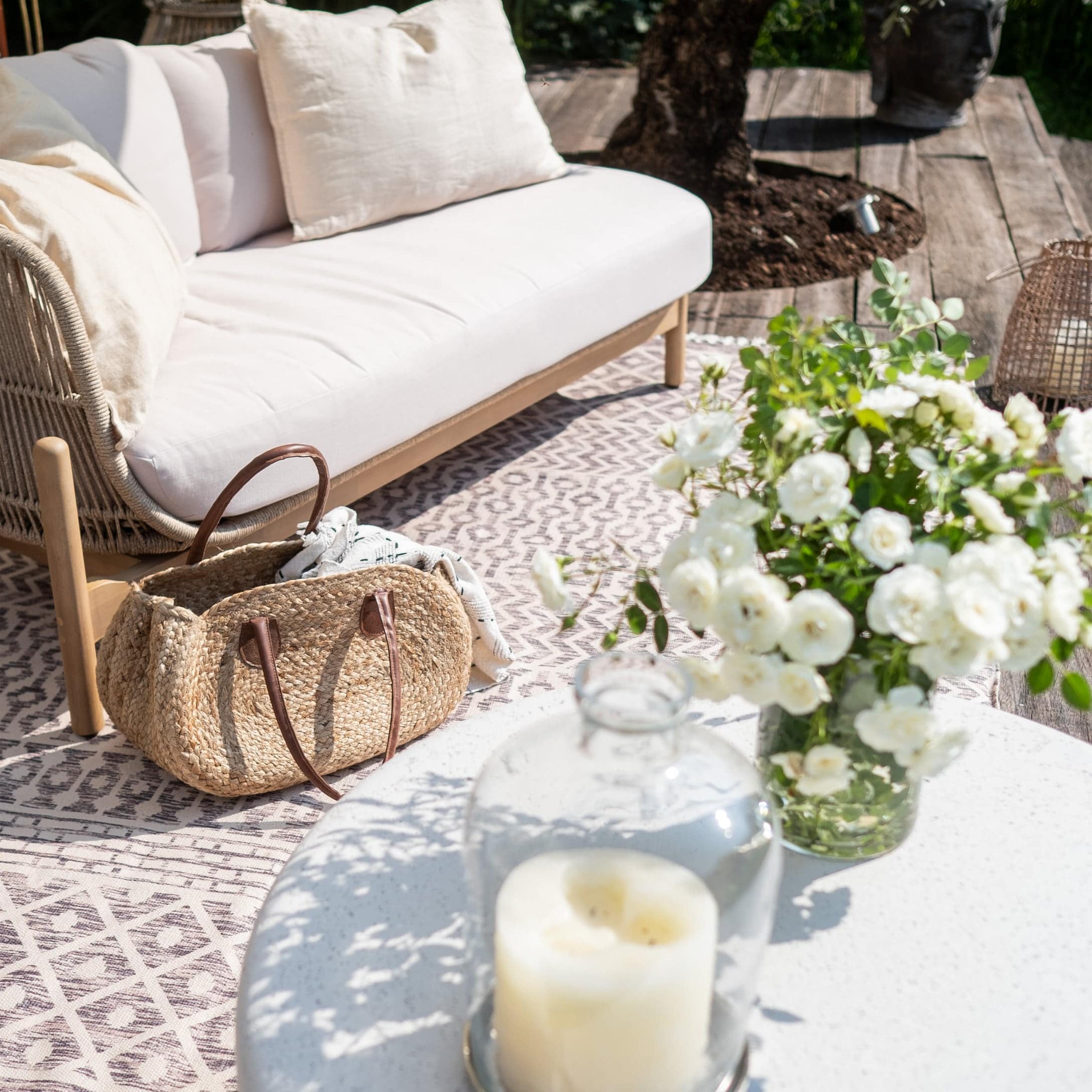 Comfortabele witte stoel met kussens buiten, rieten tas en verse witte bloemen op tafel