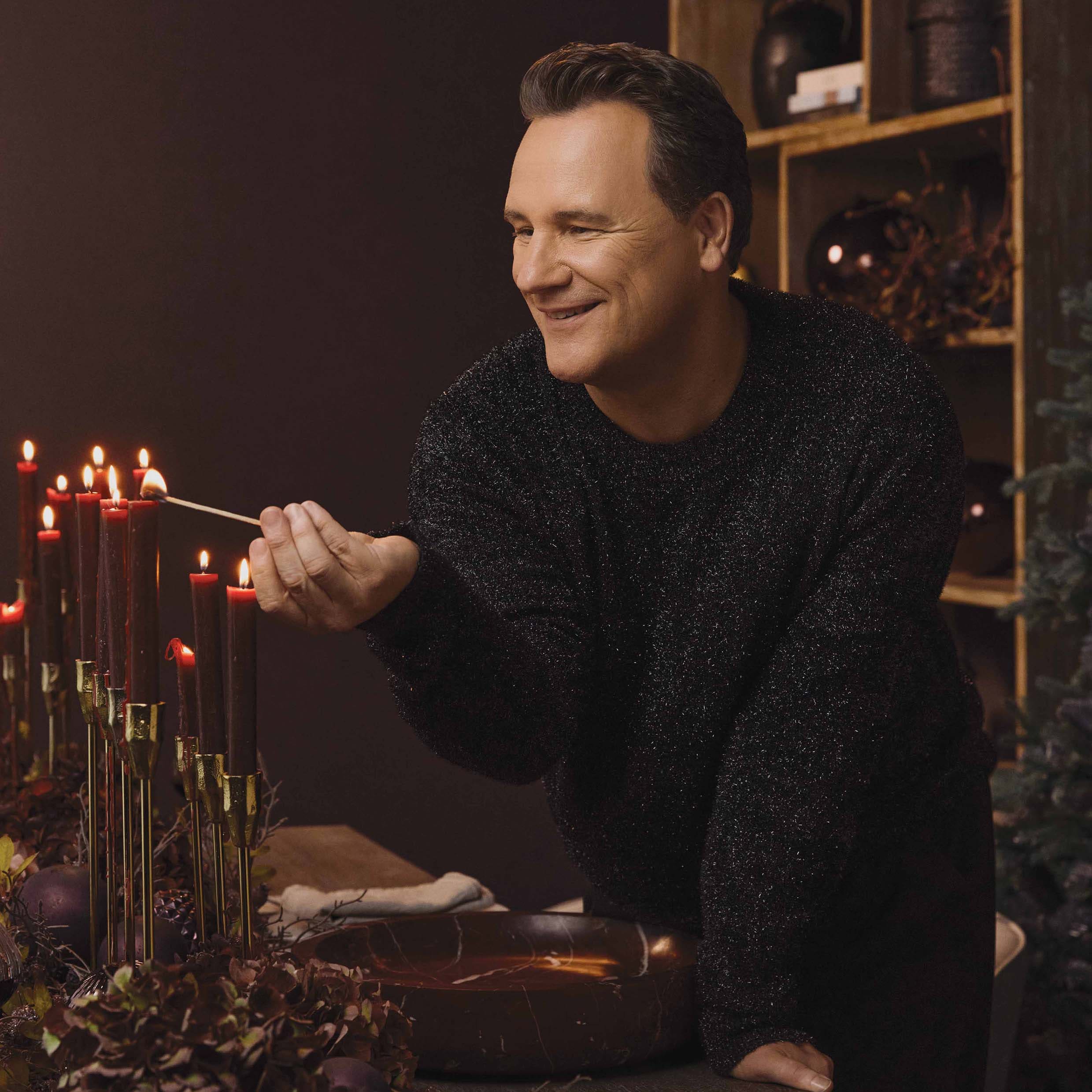 Man die rode kaarsen aansteekt op gouden kandelaars in een gezellige, gedecoreerde ruimte
