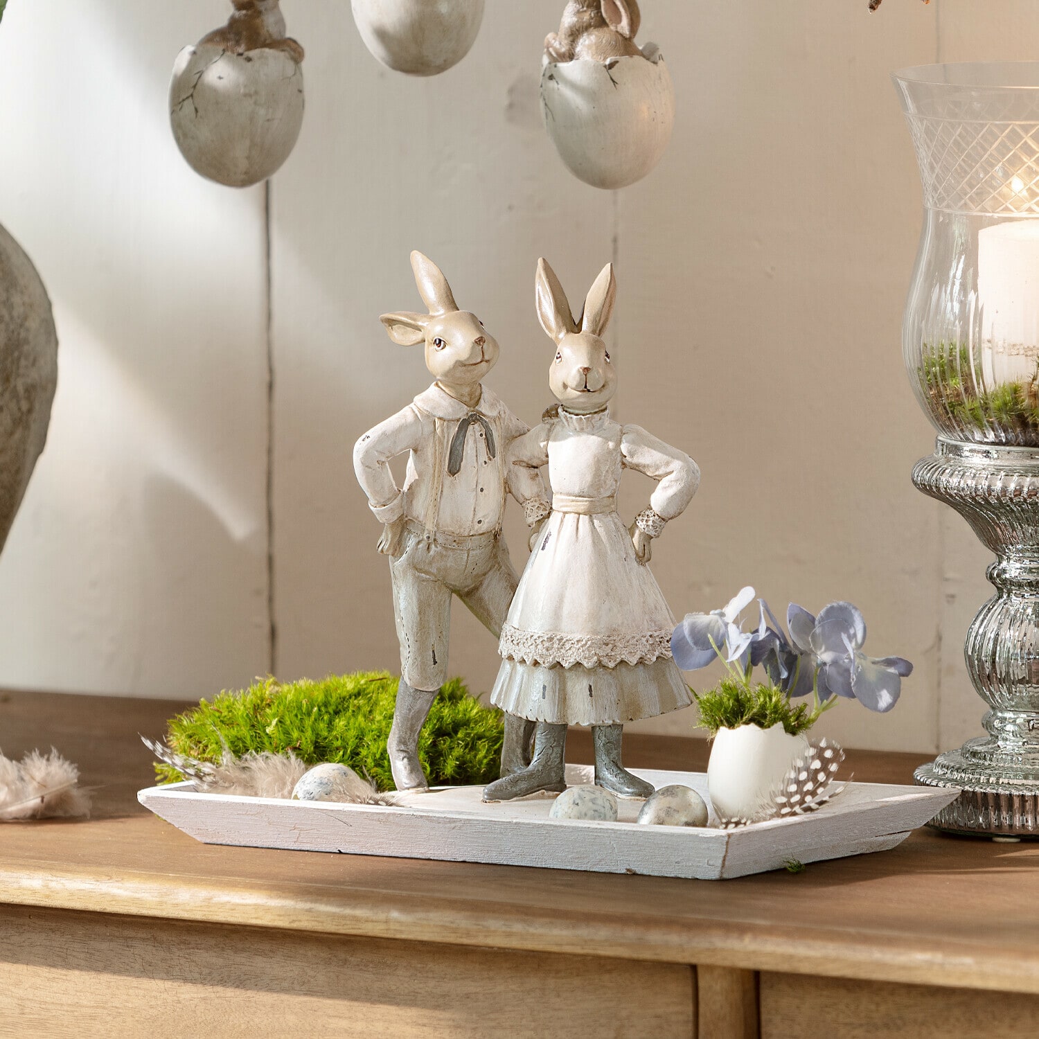 Decoratie met twee witte houten konijnen op een houten dienblad met groen mos en decoratieve eieren