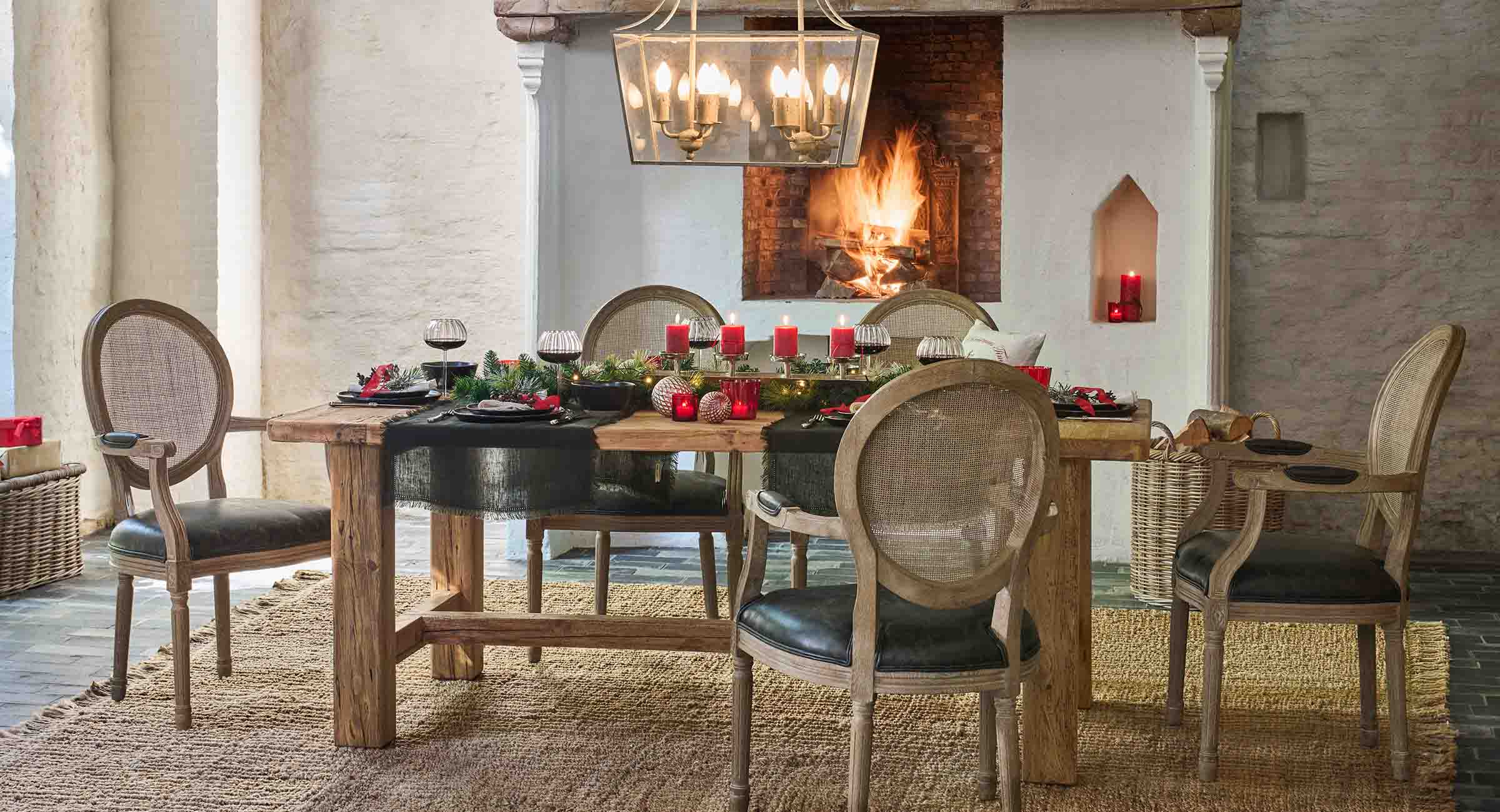 Rustieke houten tafel met natuurlijke decoraties en rode kaarsen bij een brandende open haard