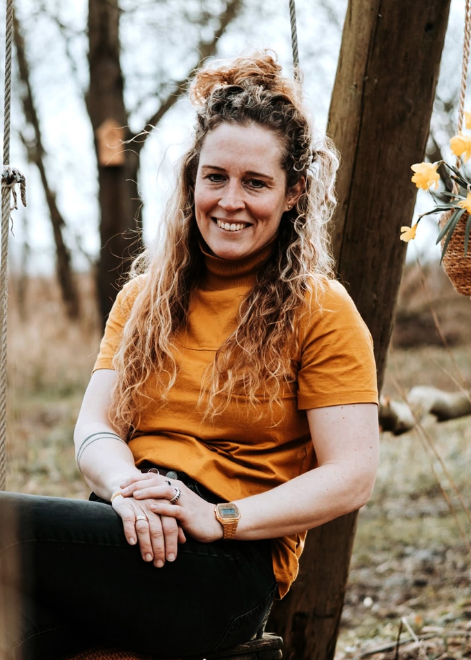 Vrouw in oranje shirt zittend op een schommel in een natuurlijke buitenomgeving