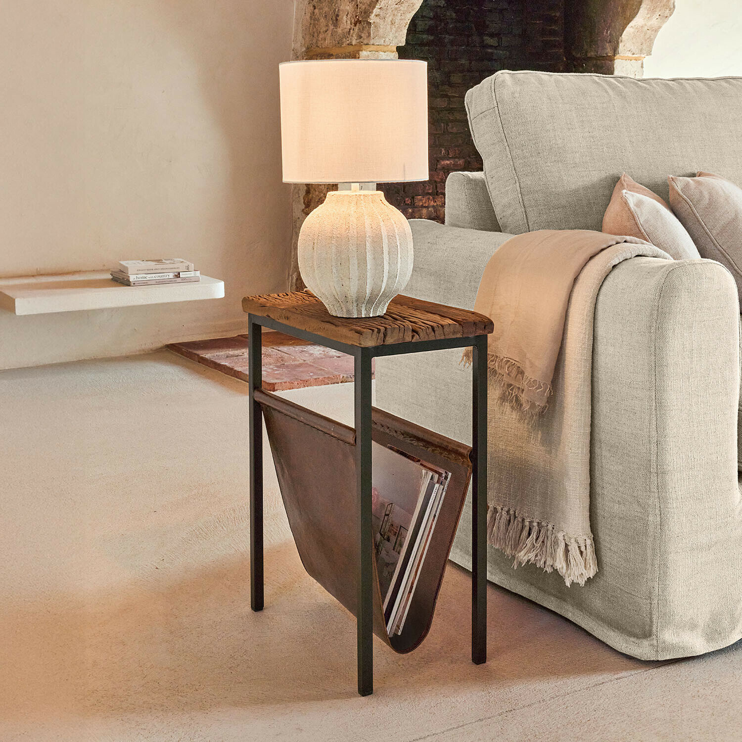Bijzettafel met houten blad en leren tijdschriftenhouder naast beige bank met tafellamp