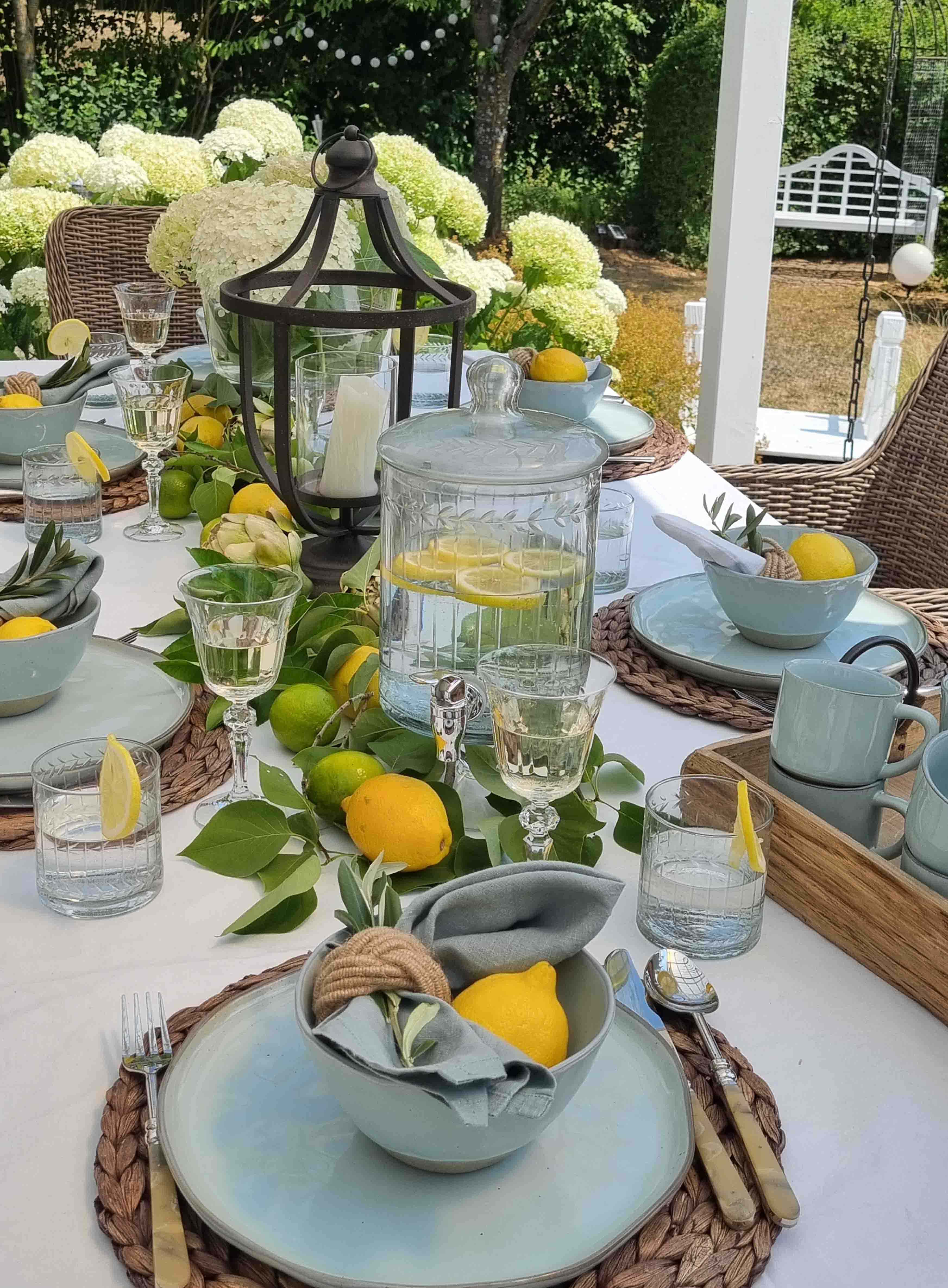 Zomerse tuintafel met blauw keramiek, citroenen en lantaarn, witte hortensia's op de achtergrond