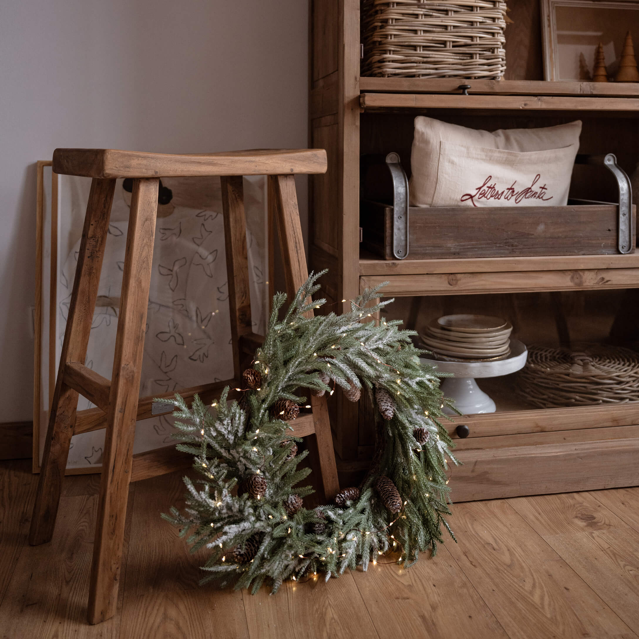 Decoratieve kerstkrans met groene takken en dennenappels op houten vloer naast een kruk