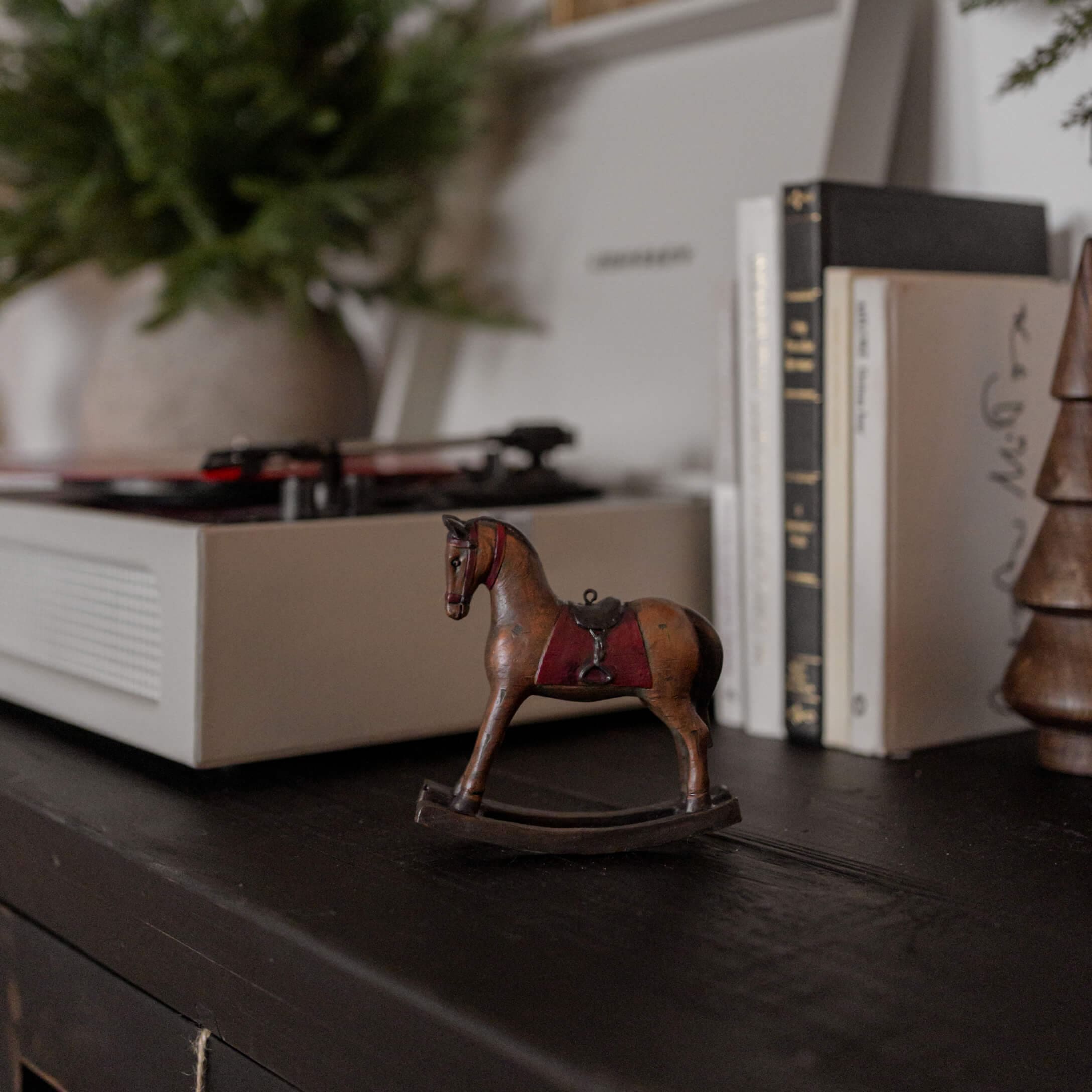 Bruin houten hobbelpaard met rood zadel op zwart oppervlak naast boeken en platenspeler