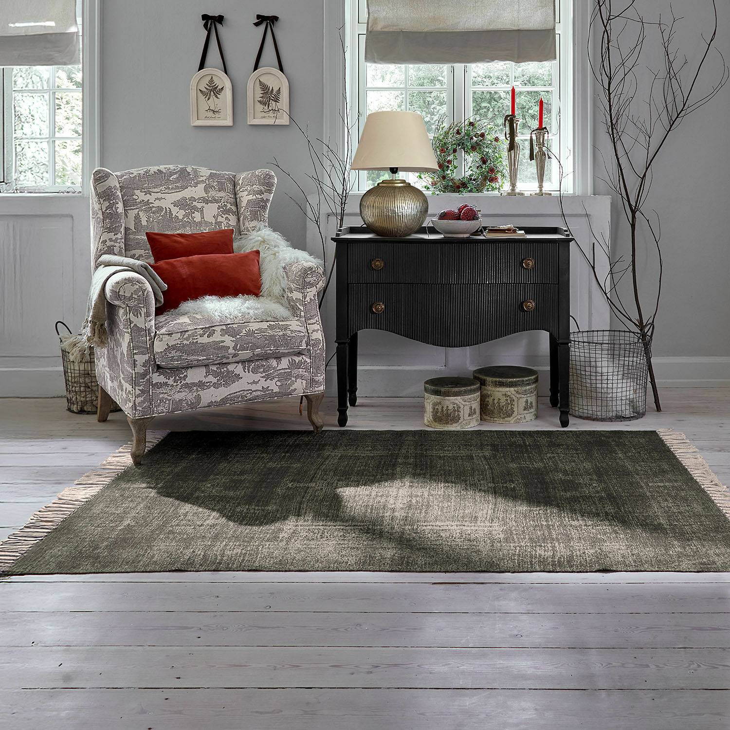 Gezellige grijs-witte fauteuil met rode kussens naast zwarte vintage ladekast in woonkamer