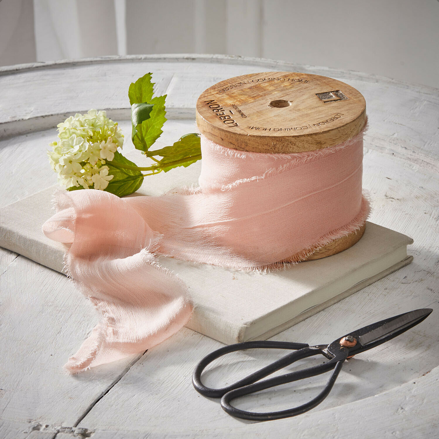 Roze stoffen lint op houten spoel met schaar en bloem op witte tafel