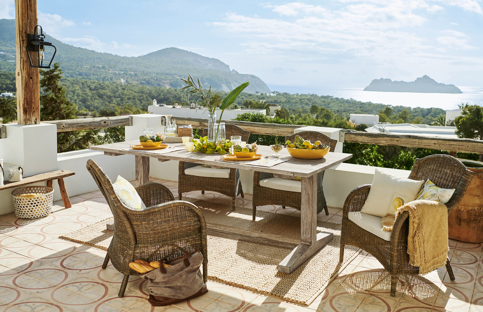 Terras met rotanmeubilair en lichte houten tafel met uitzicht op zee en bergen, mediterrane stijl